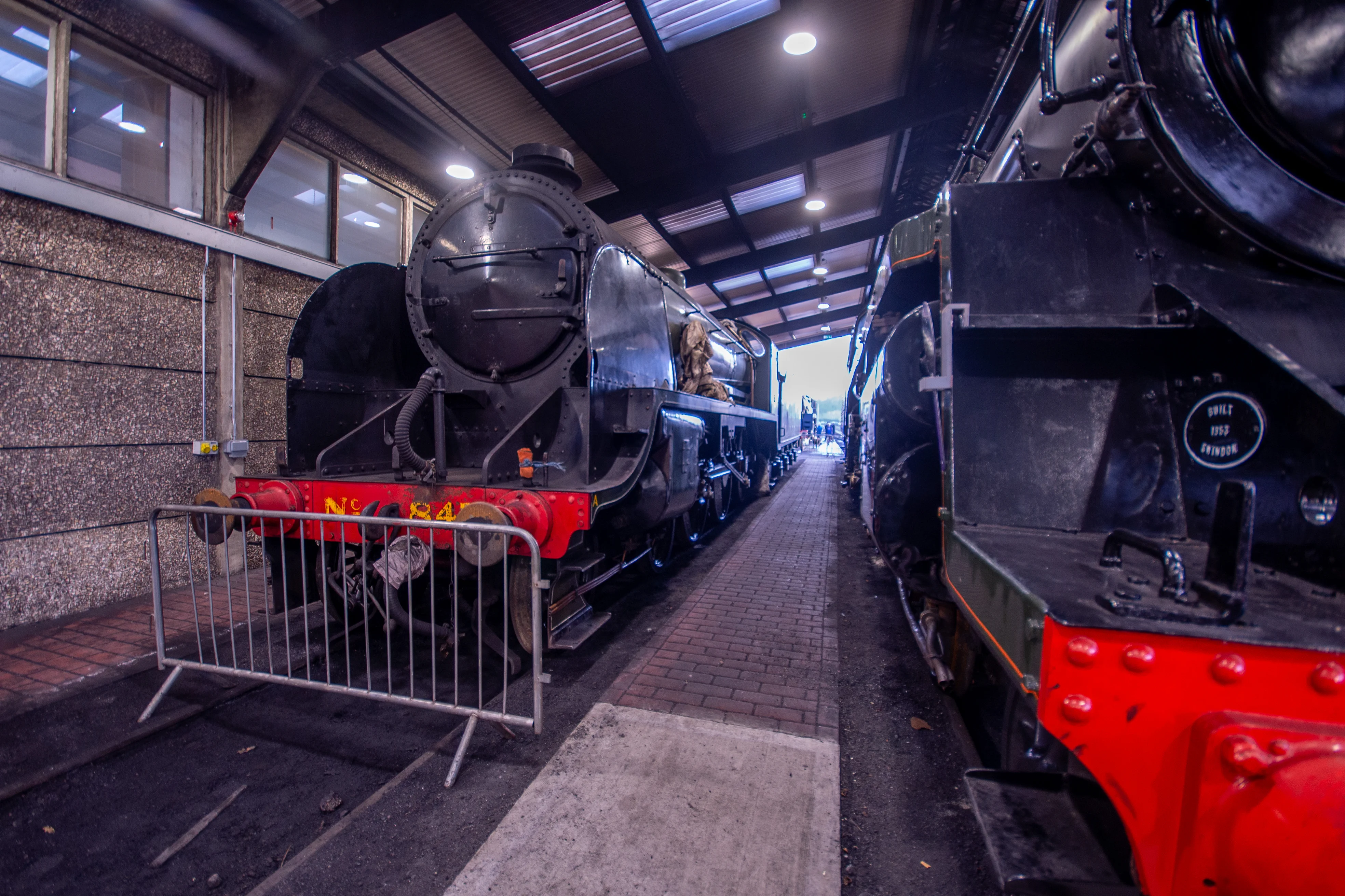Steam locomotive cab interior showing pressure gauges, brass pipes, valves and a red regulator lever.