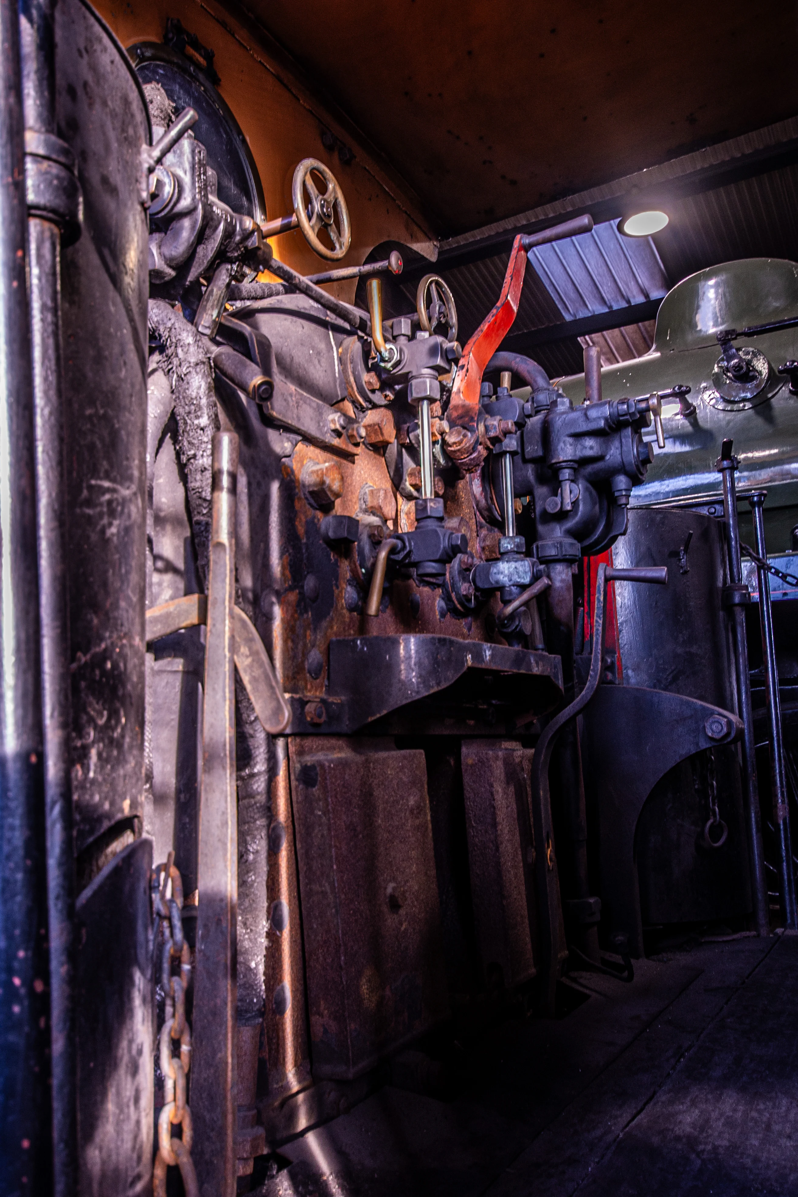 Steam locomotive cab interior showing pressure gauges, brass pipes, valves and a red regulator lever.