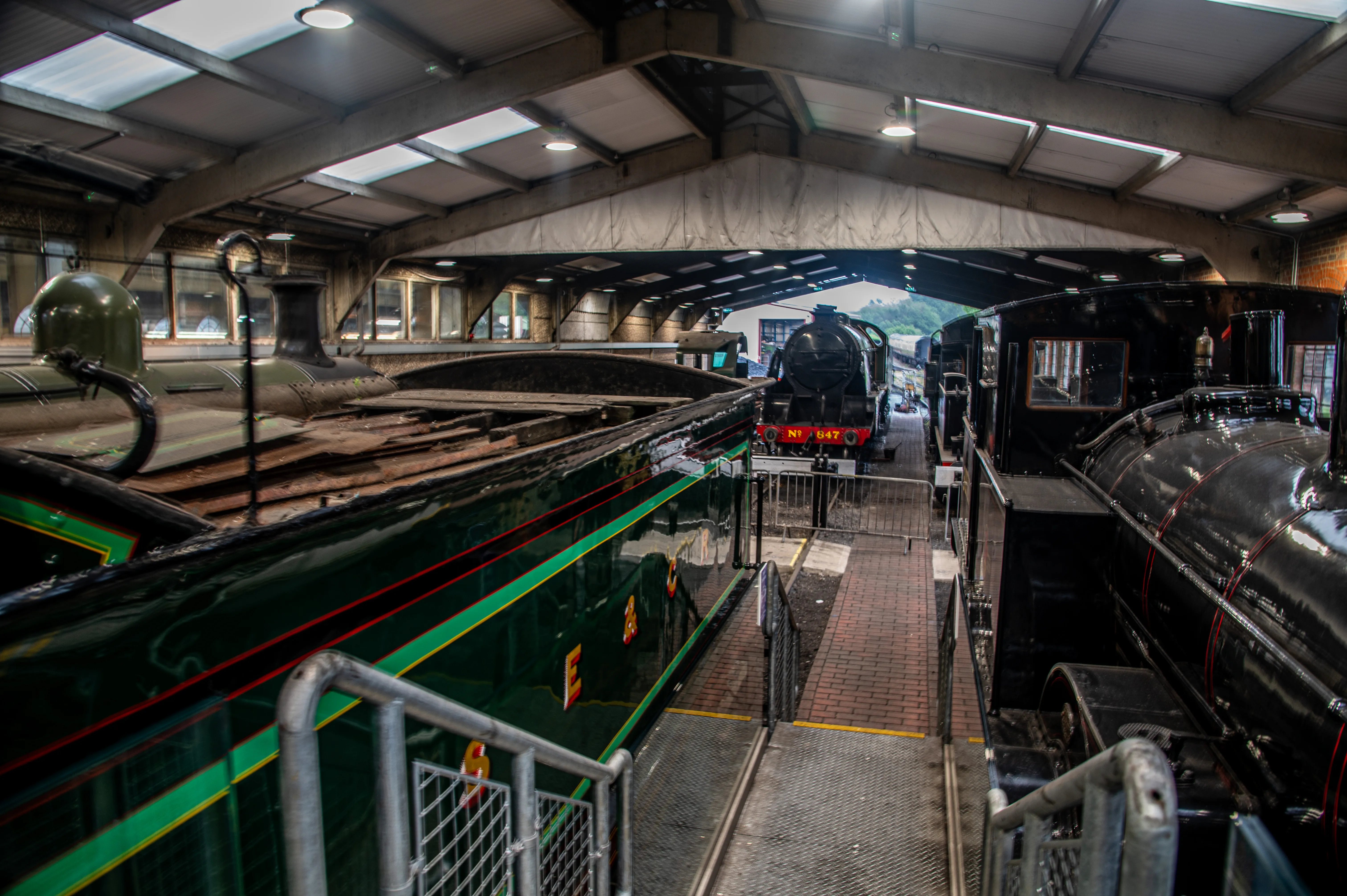 Steam locomotive cab interior showing pressure gauges, brass pipes, valves and a red regulator lever.