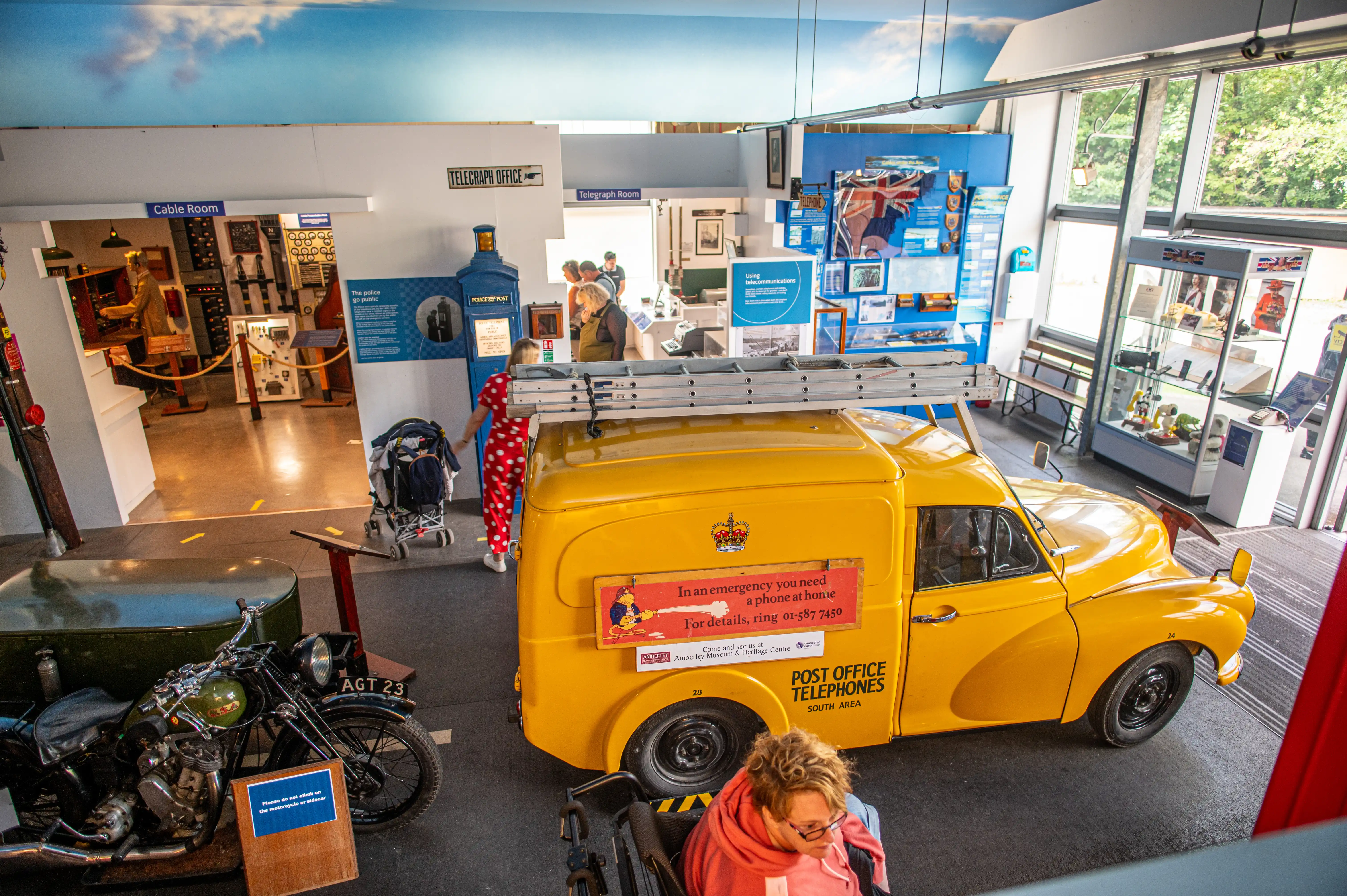 Yellow Post Office Telephones van in a museum with vintage motorcycle and historic telecommunications displays.