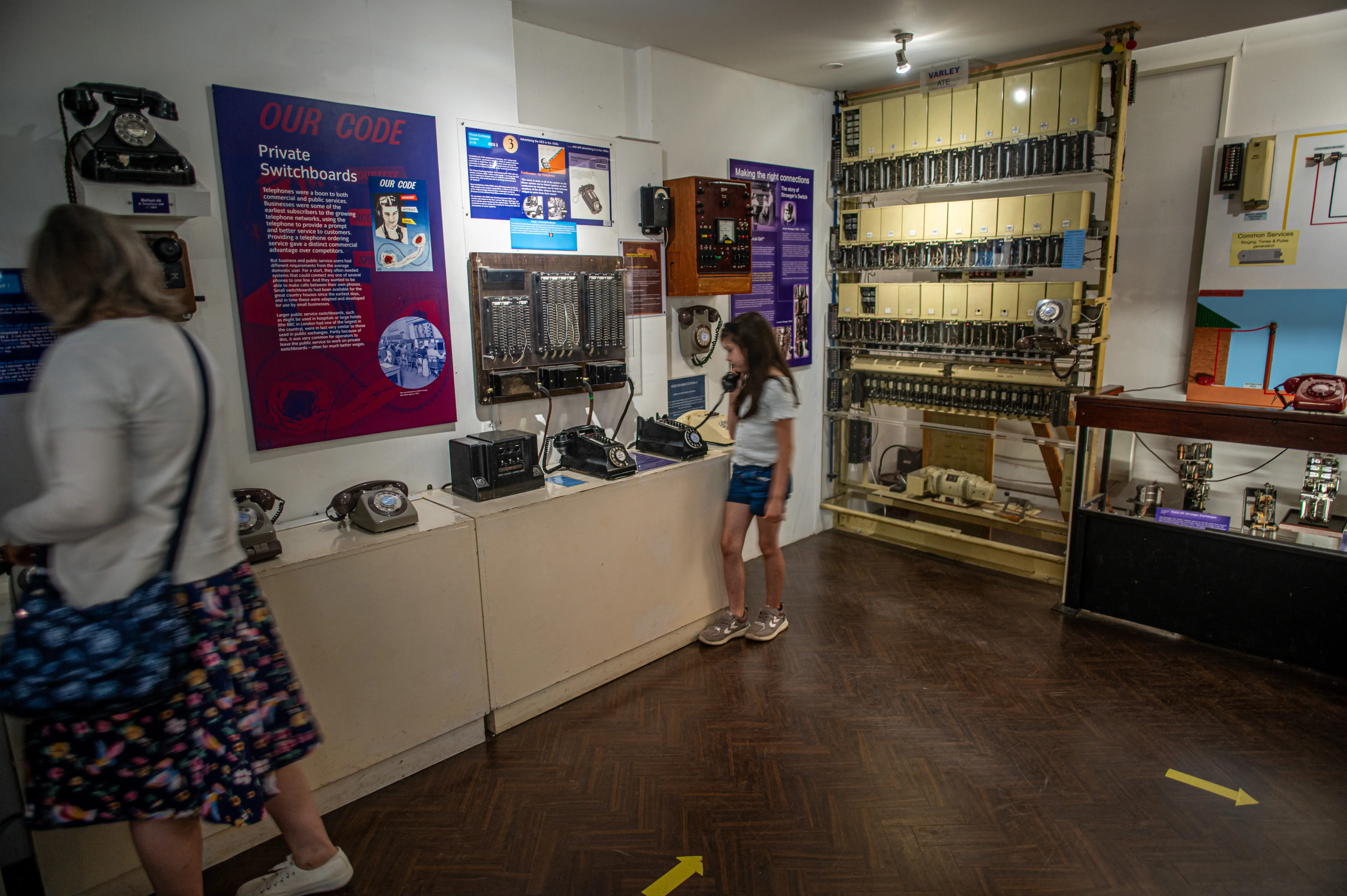  A museum exhibit displays vintage telephone switchboards and equipment, with a young girl interacting with a telephone.