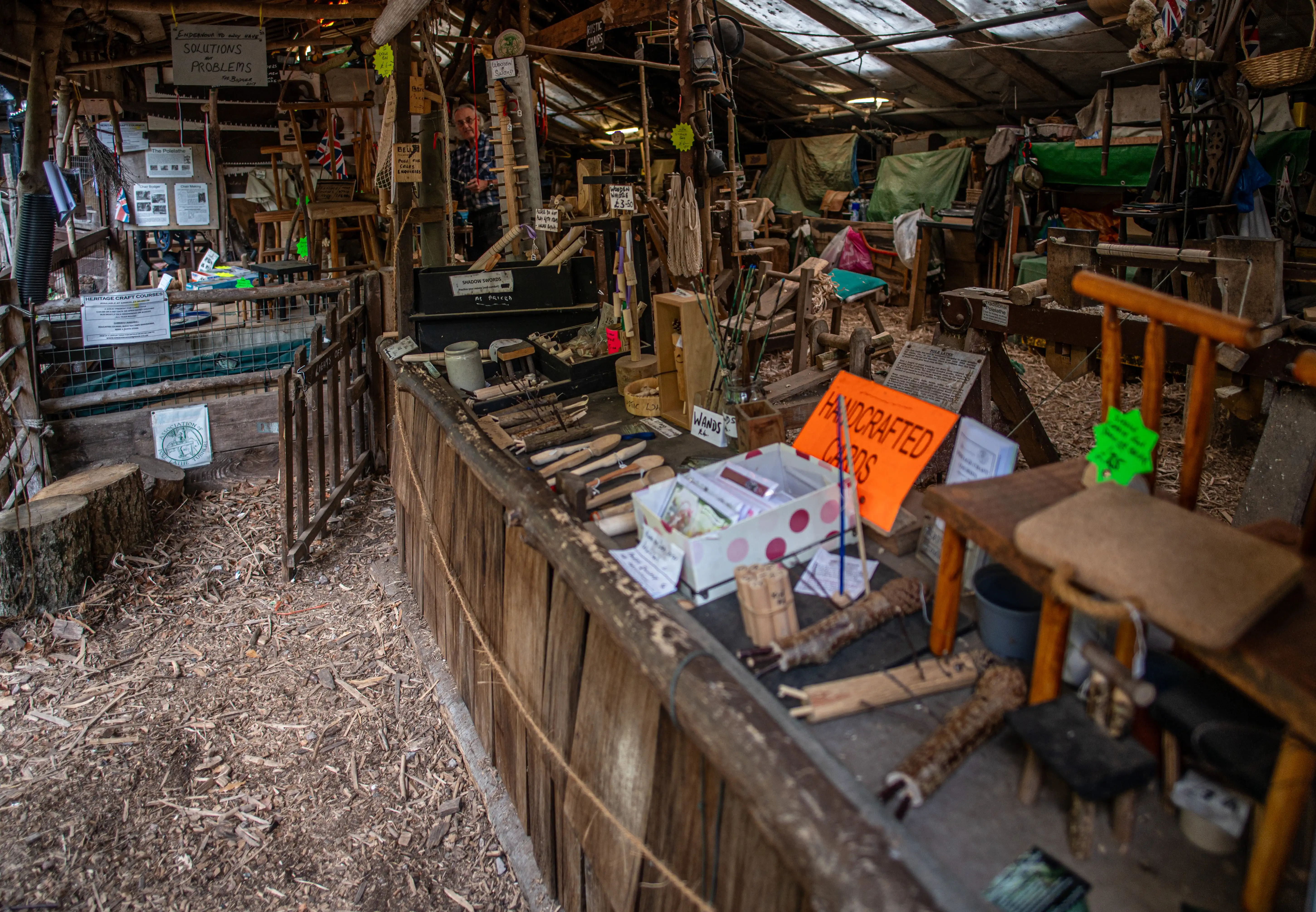 Interior view of a rustic workshop with wooden beams, a tin roof, and various handcrafted items displayed on a counter.