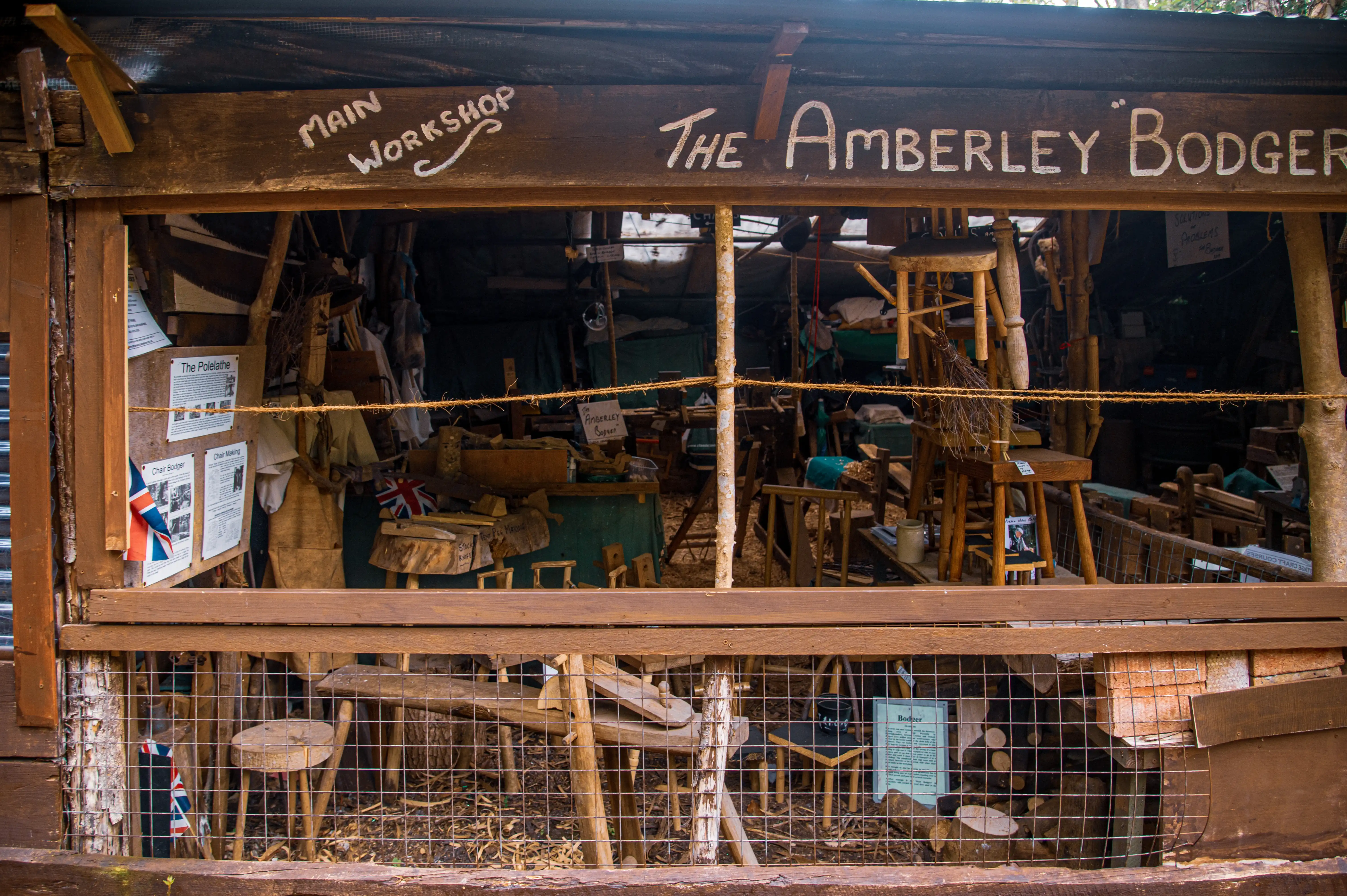 An outdoor rustic shop constructed from wood and corrugated iron, with a wooden gate and a bicycle visible. The shop is surrounded by trees and greenery.