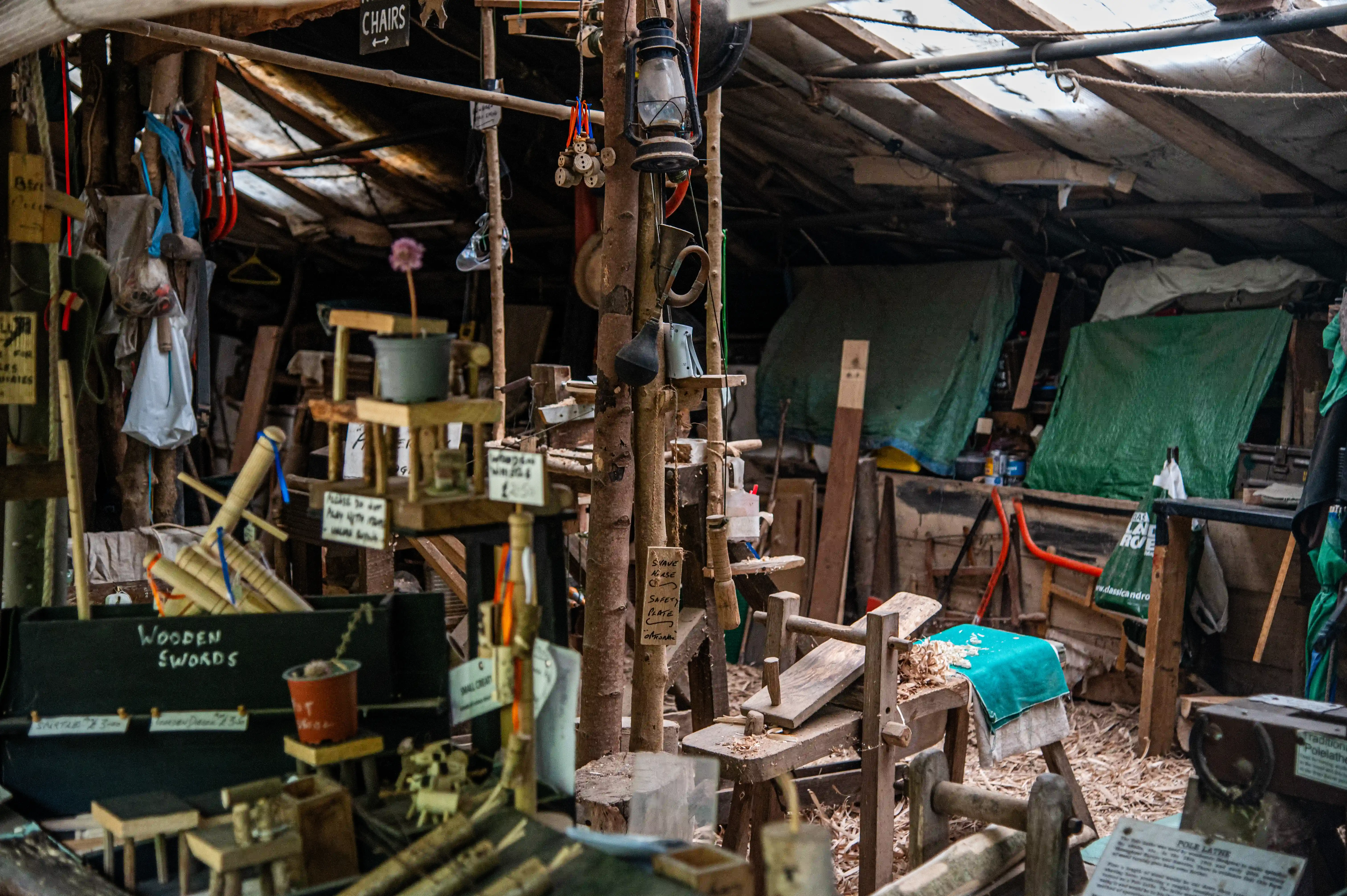 A dimly lit, rustic workshop interior filled with wooden crafts, tools, and hanging lanterns. A sign reads 