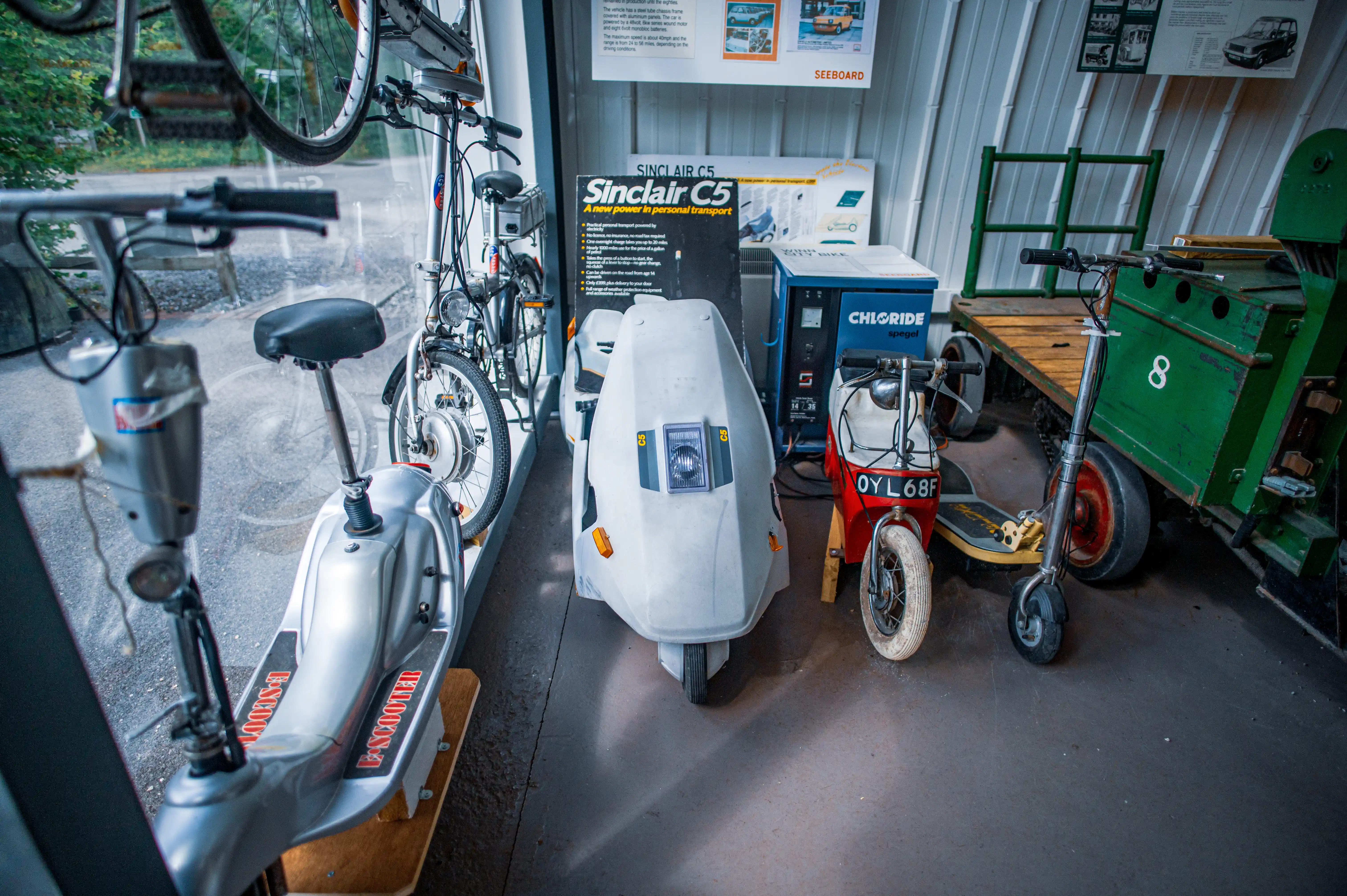 A display of vintage electric personal transport vehicles, featuring a Sinclair C5, two scooters and a bicycle.