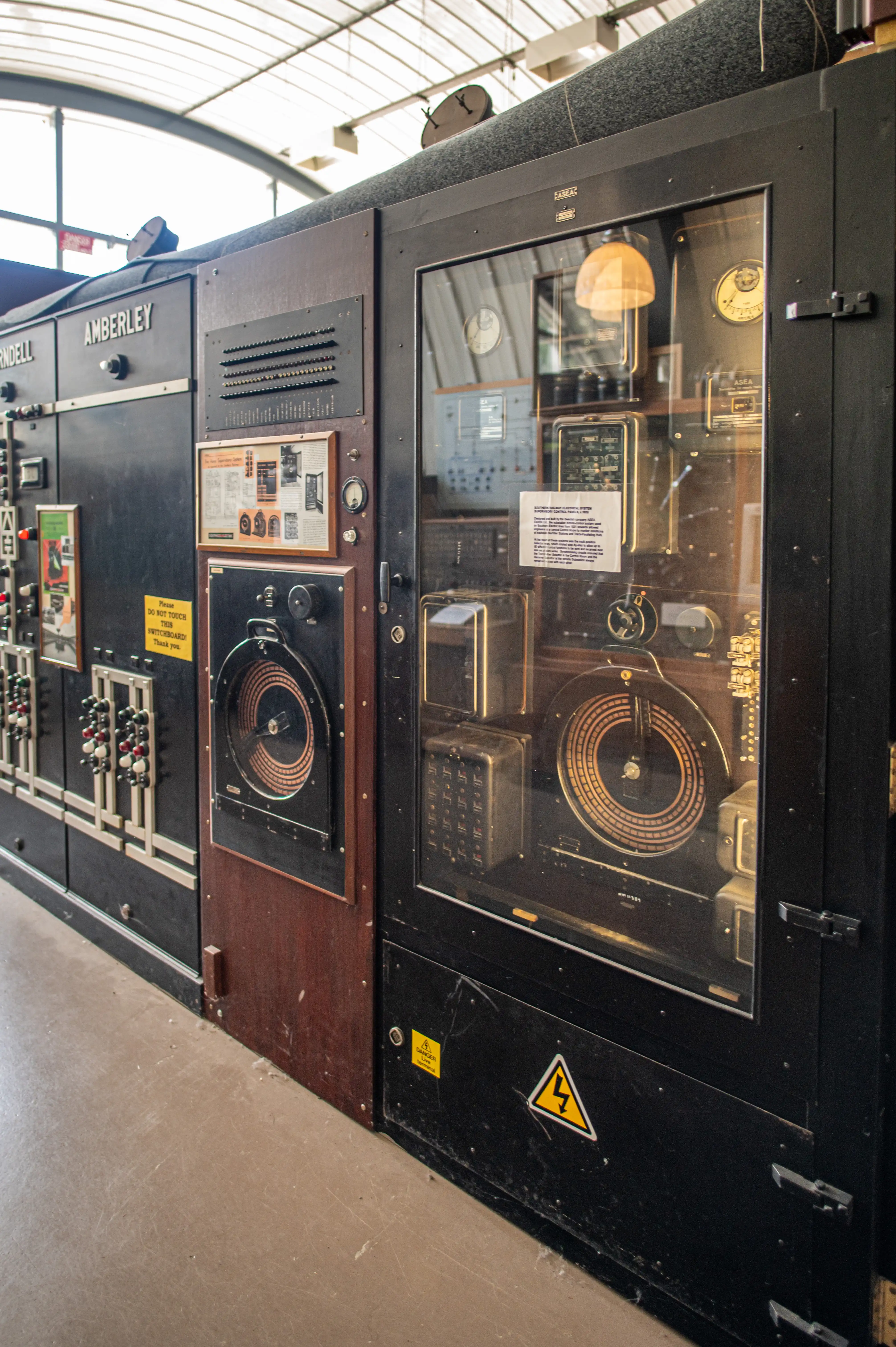 A detailed view of a section of an old, large electrical control panel, with the name 'AMBERLEY'
                               prominently displayed. The panel features glass windows revealing complex internal components, including circular dials, meters, and numerous electrical parts.