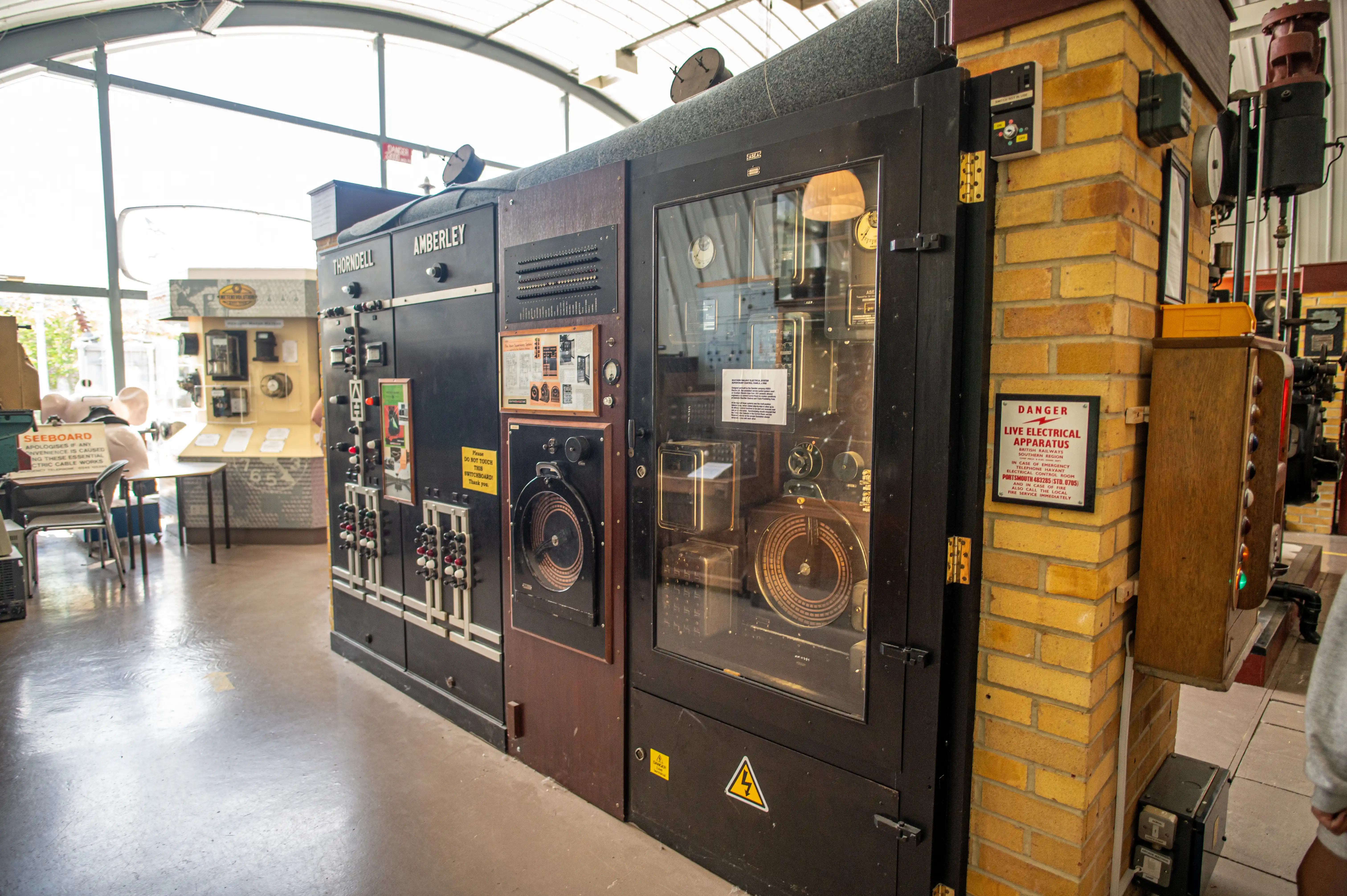 Vintage electrical control panel with switches, gauges, hazard signs, and museum display boards in a technical exhibit.