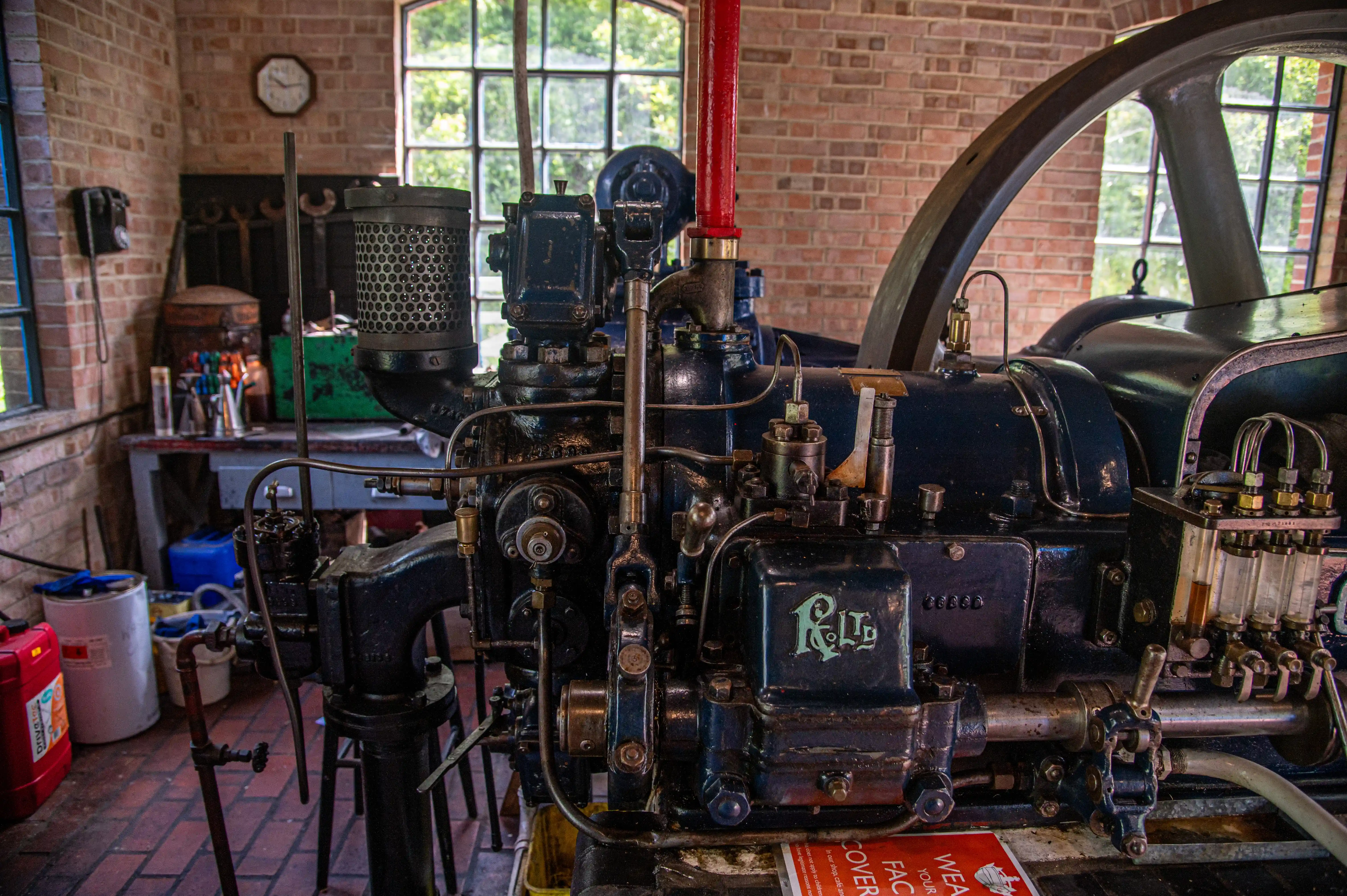 Dark-blue stationary engine with RL Ltd branding in a brick workshop with tools, windows, and workbench.