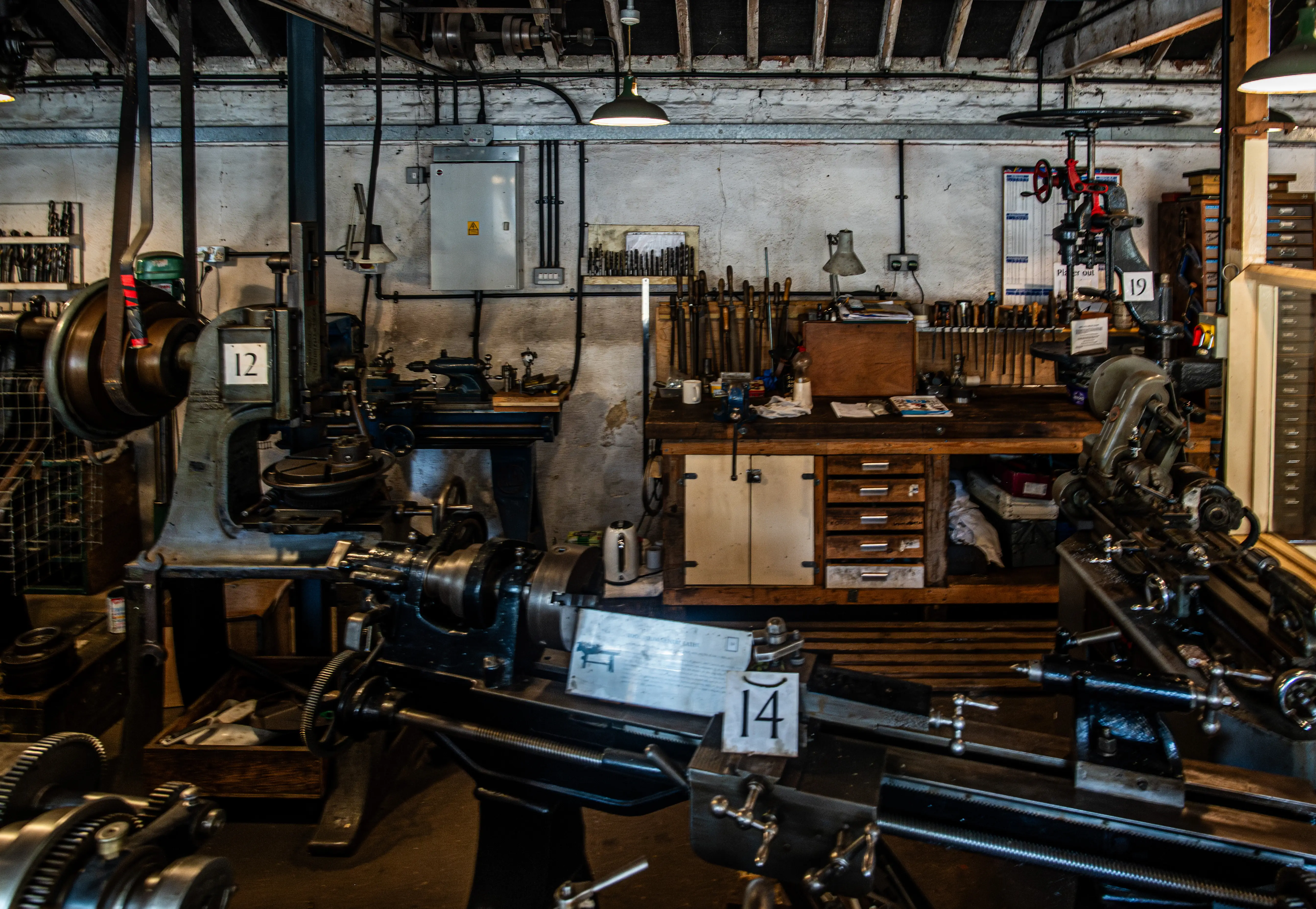 Interior view of a well-equipped vintage workshop with multiple metal lathes and a workbench filled with tools.
