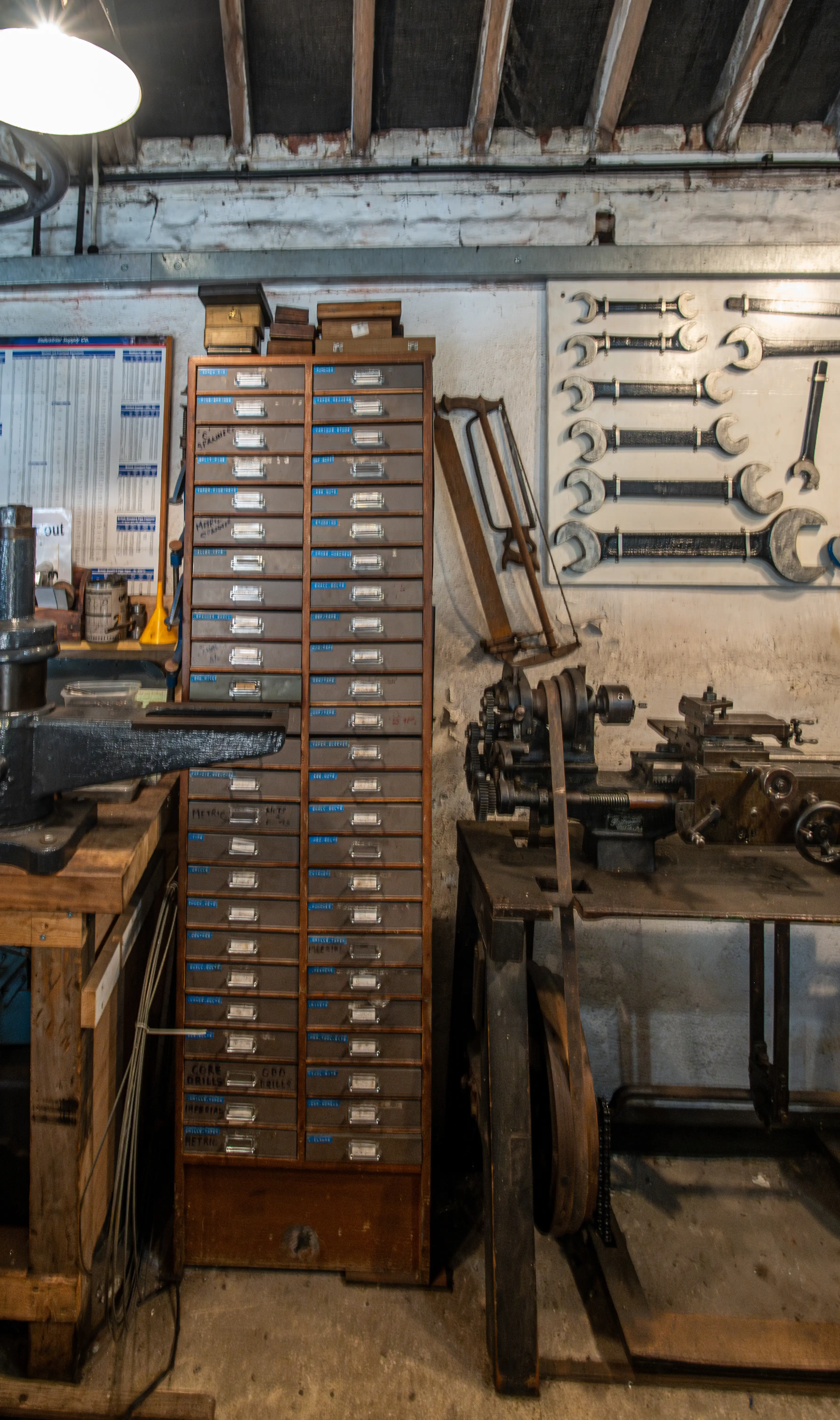 Workshop with labelled tool cabinet, wall-mounted wrenches and tools, and two metalworking machines including a lathe.
