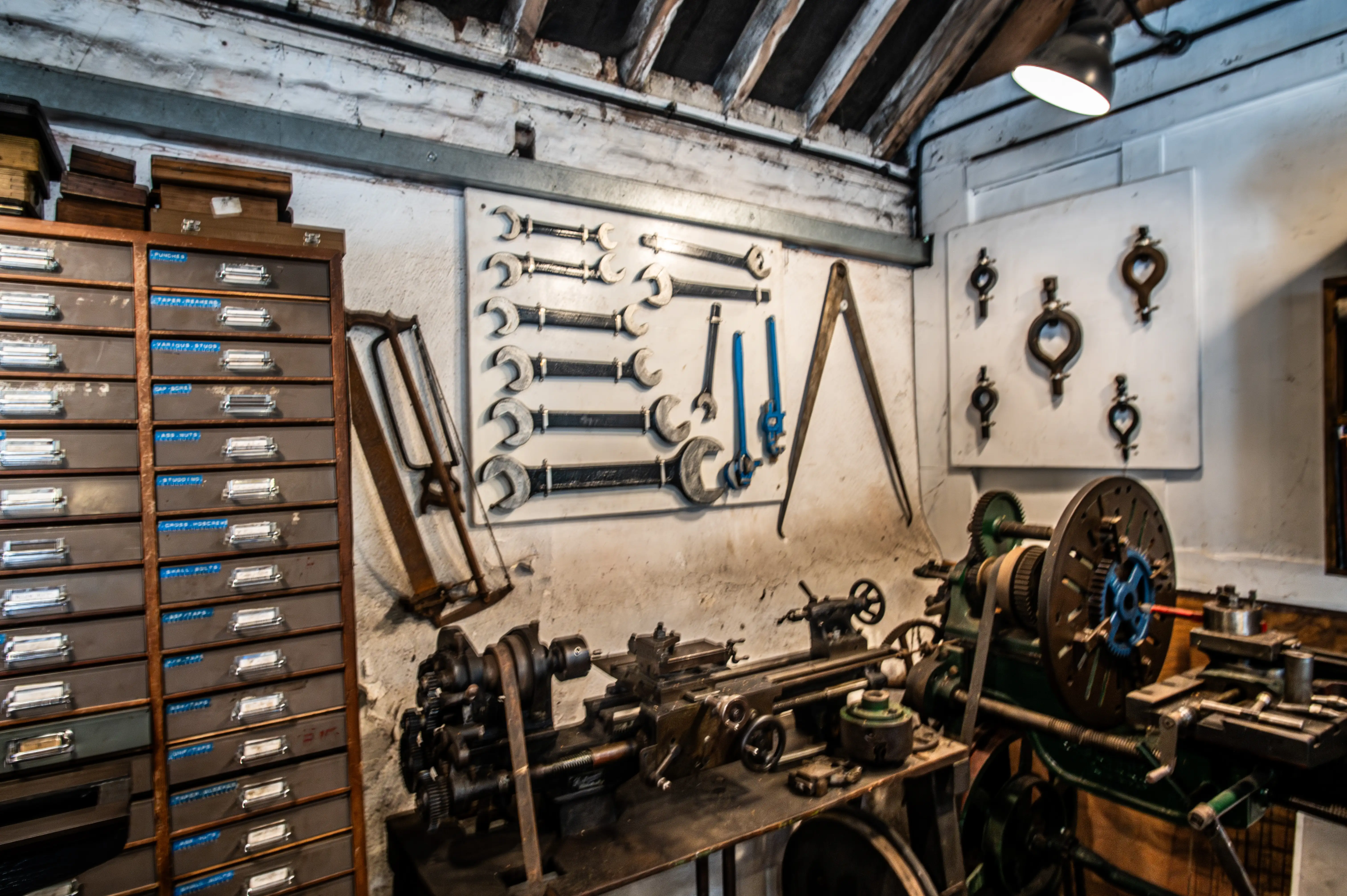 Workshop with labelled tool cabinet, wall-mounted wrenches and tools, and two metalworking machines including a lathe.