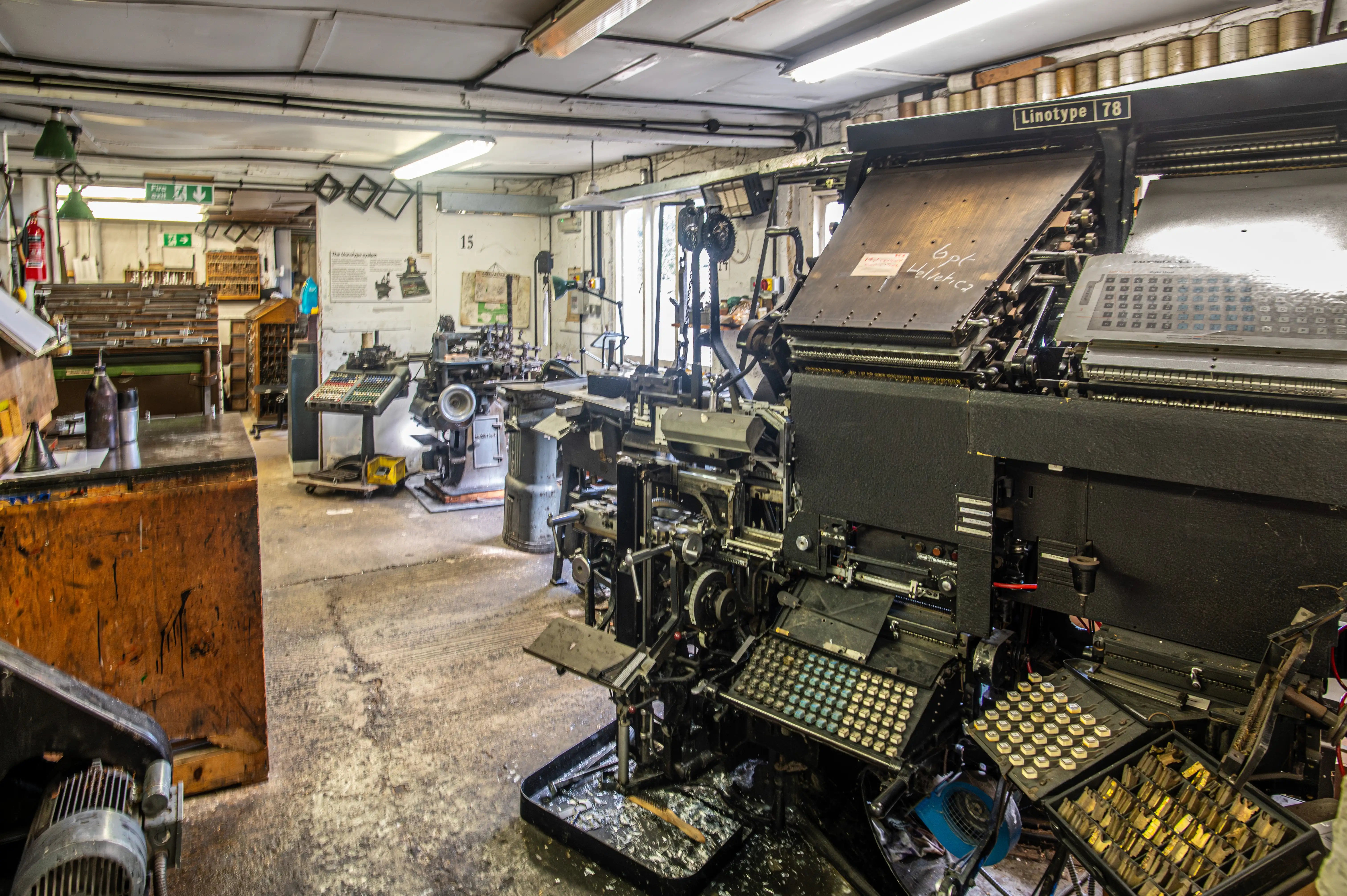 Traditional print workshop with Linotype machine, workbenches, tools, and diagrams explaining printing processes.