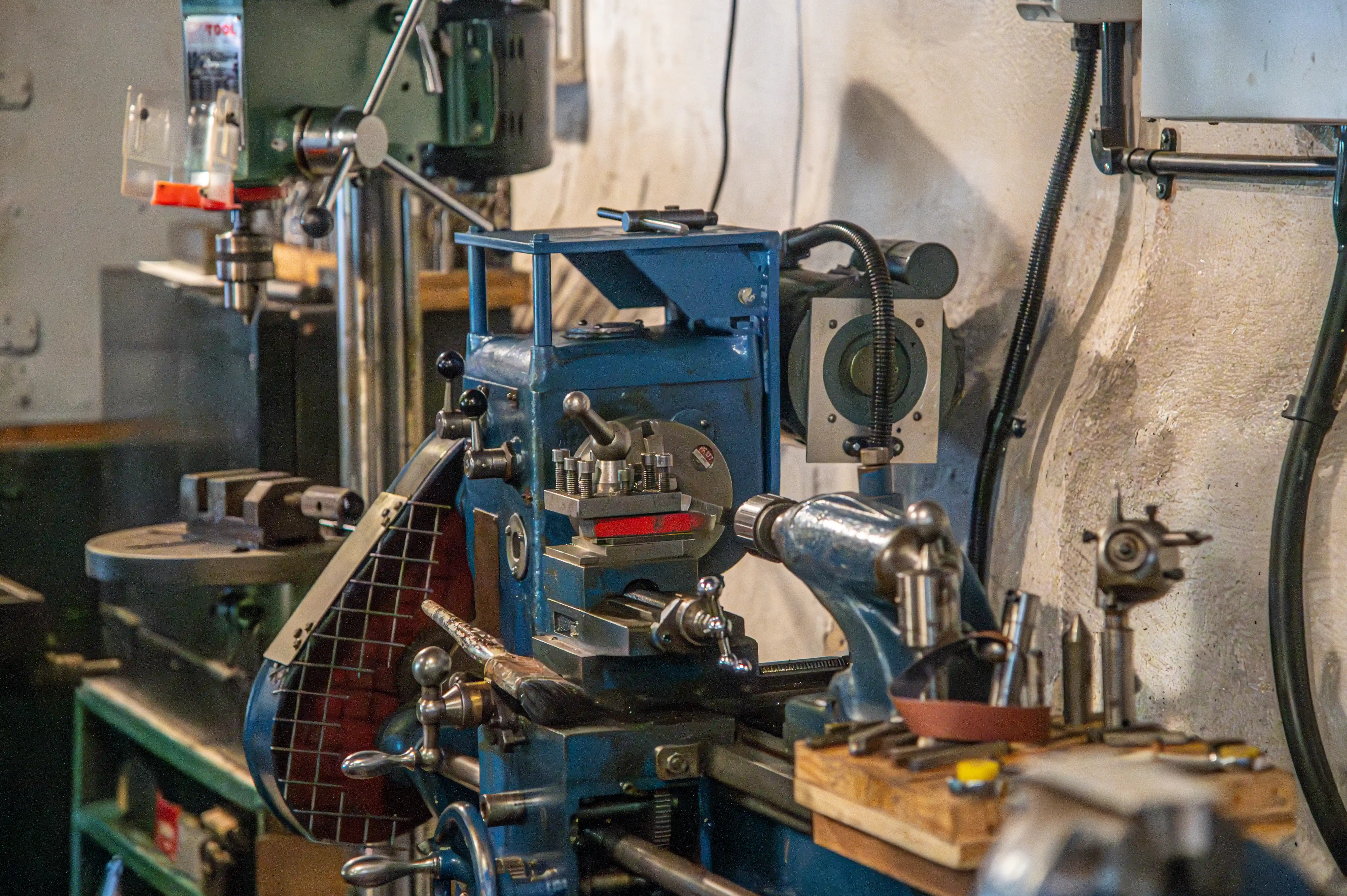 Blue metal lathe and green drill press in a traditional workshop with tools and electrical fittings on the wall.
