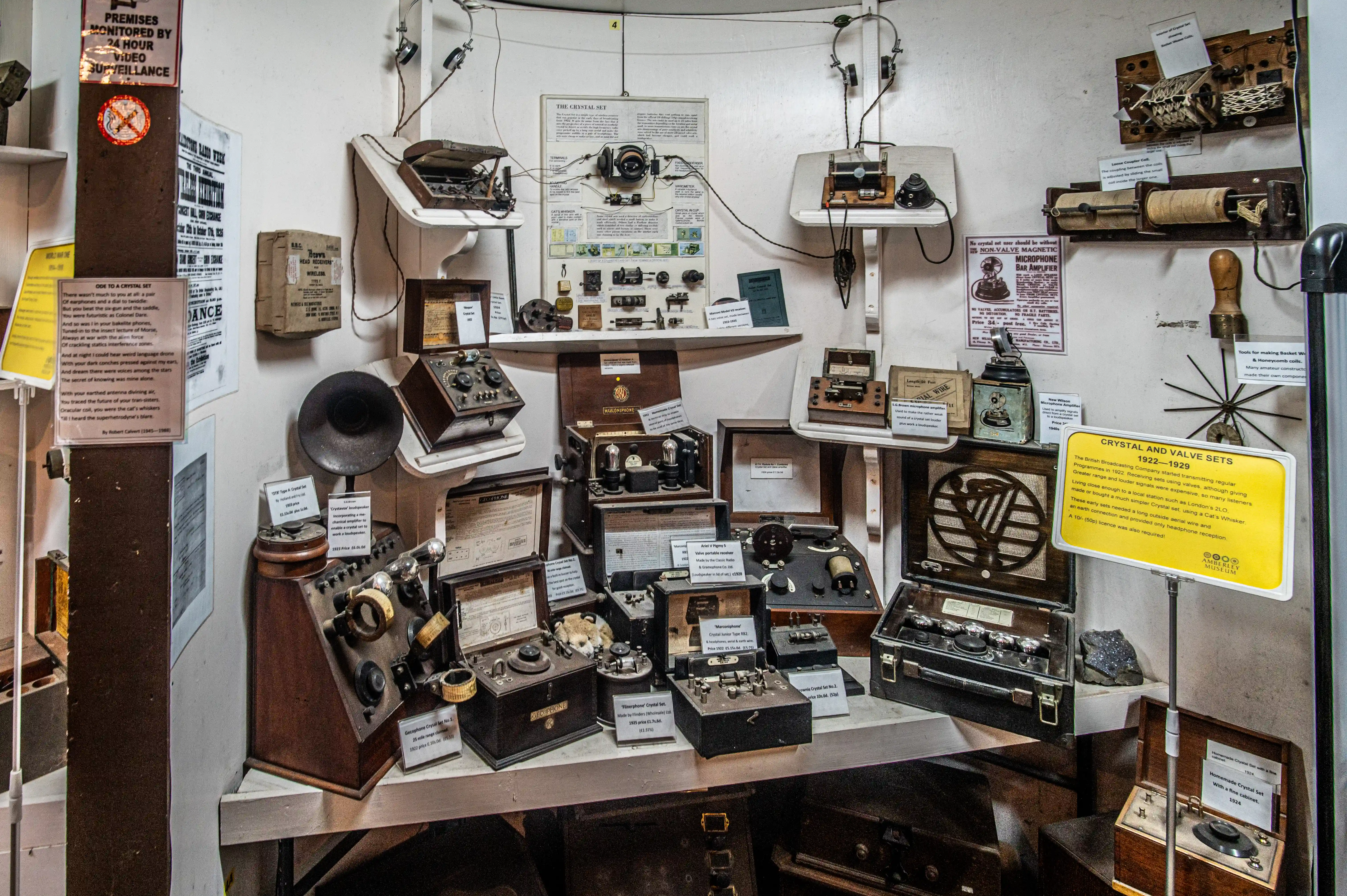 Exhibit of early radio equipment with crystal sets, valve sets, amplifiers, headphones, coils, and a yellow sign labelled “Crystal and Valve Sets 1922–1929.”