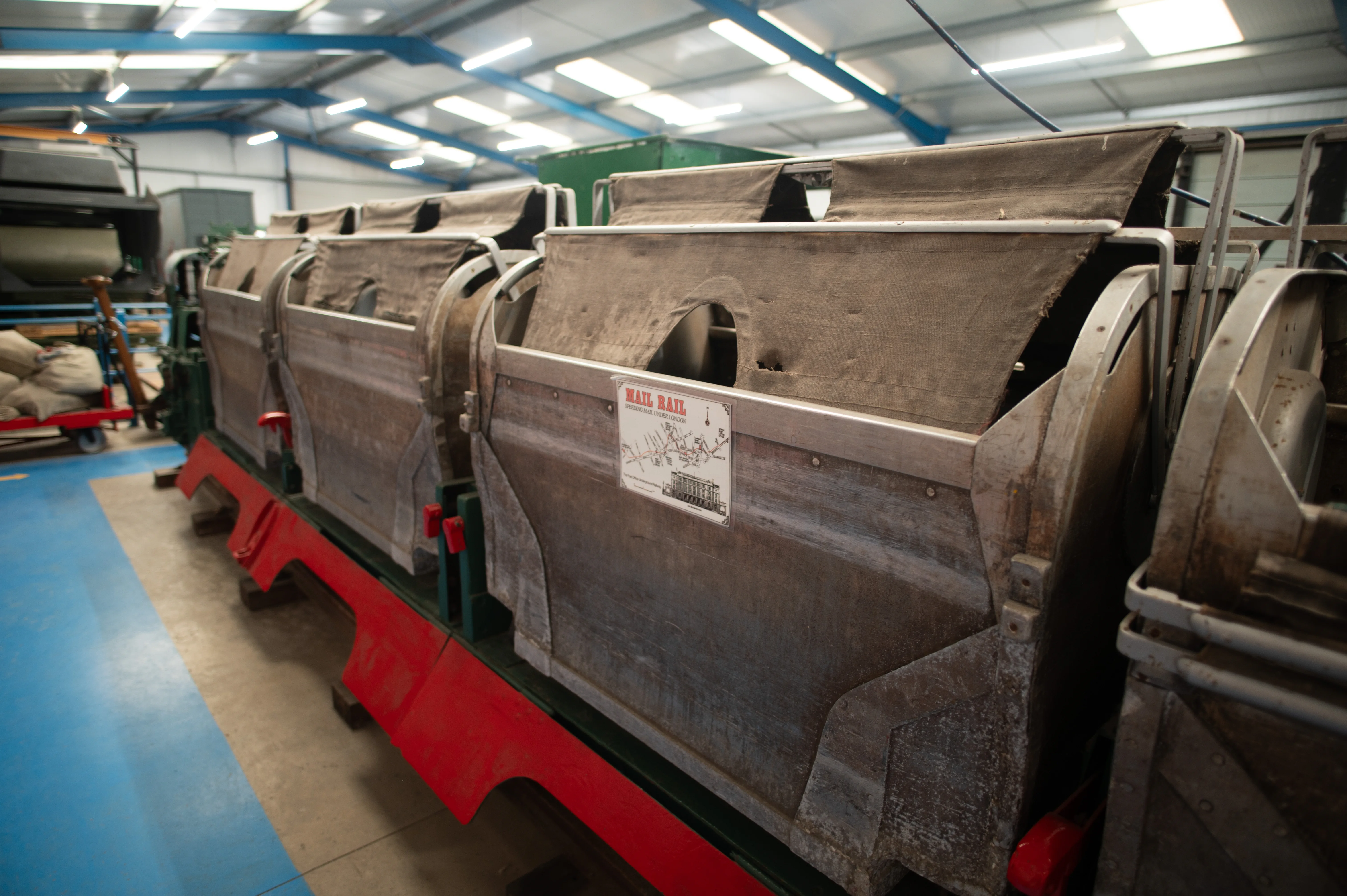Close-up view of several weathered wooden and canvas Mail Rail wagons, one with a historical map and illustration displayed on its side.