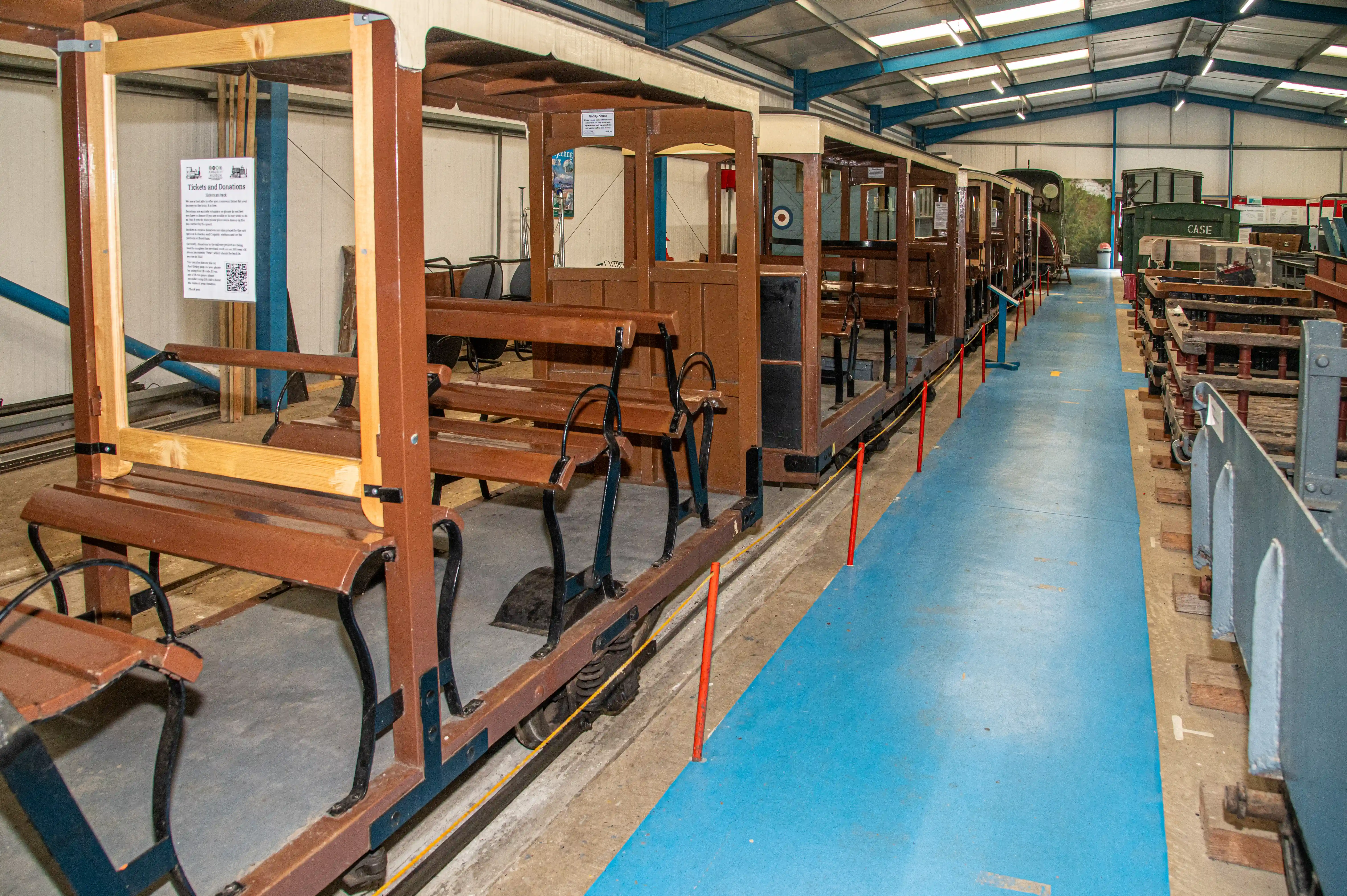 A row of old-fashioned wooden railway carriages with brown seats, displayed inside a warehouse-style building.