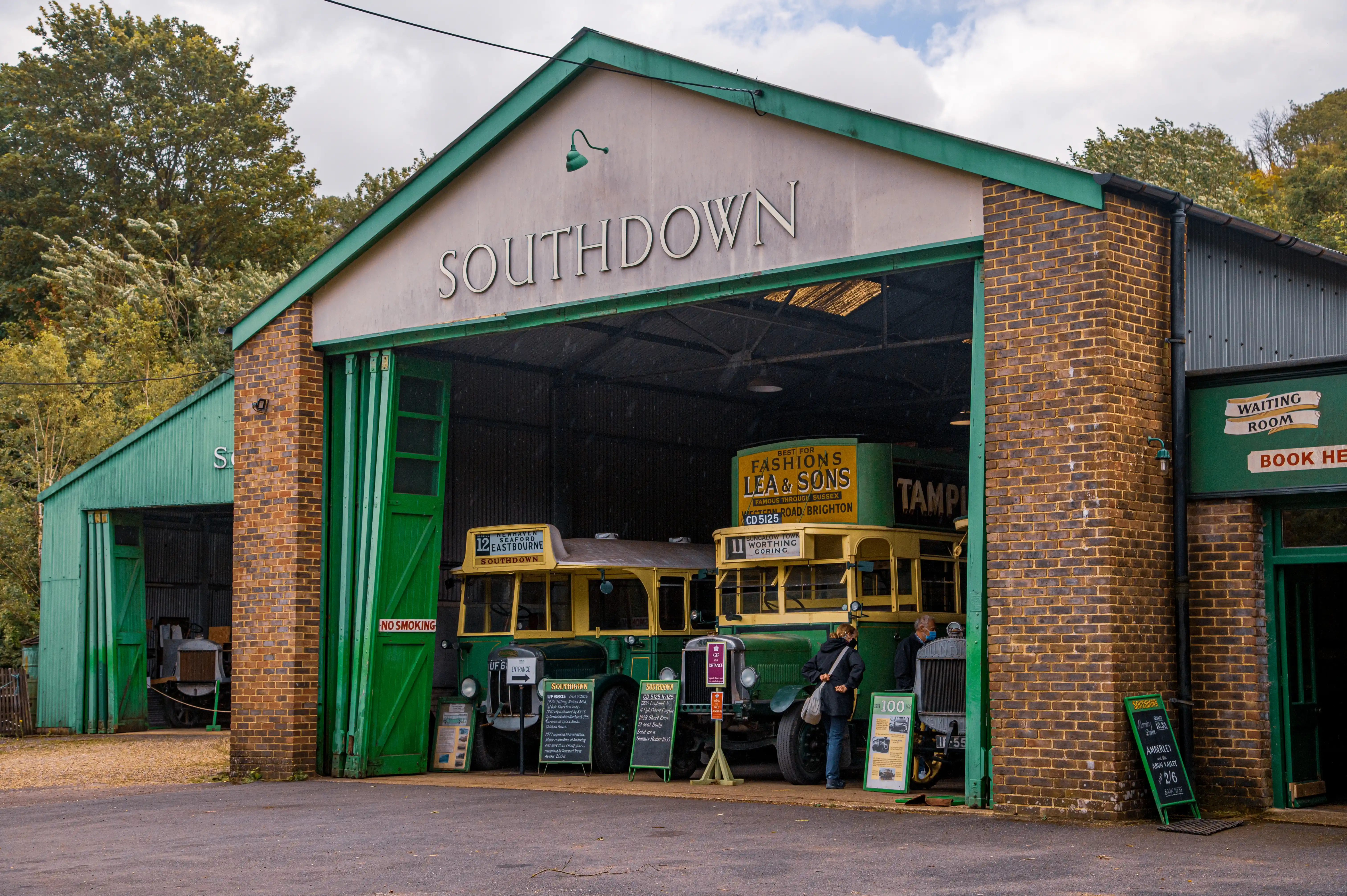 Small brick booking office painted green with Southdown Motor Services signage, chalkboard notices and a child seated on a bench.
