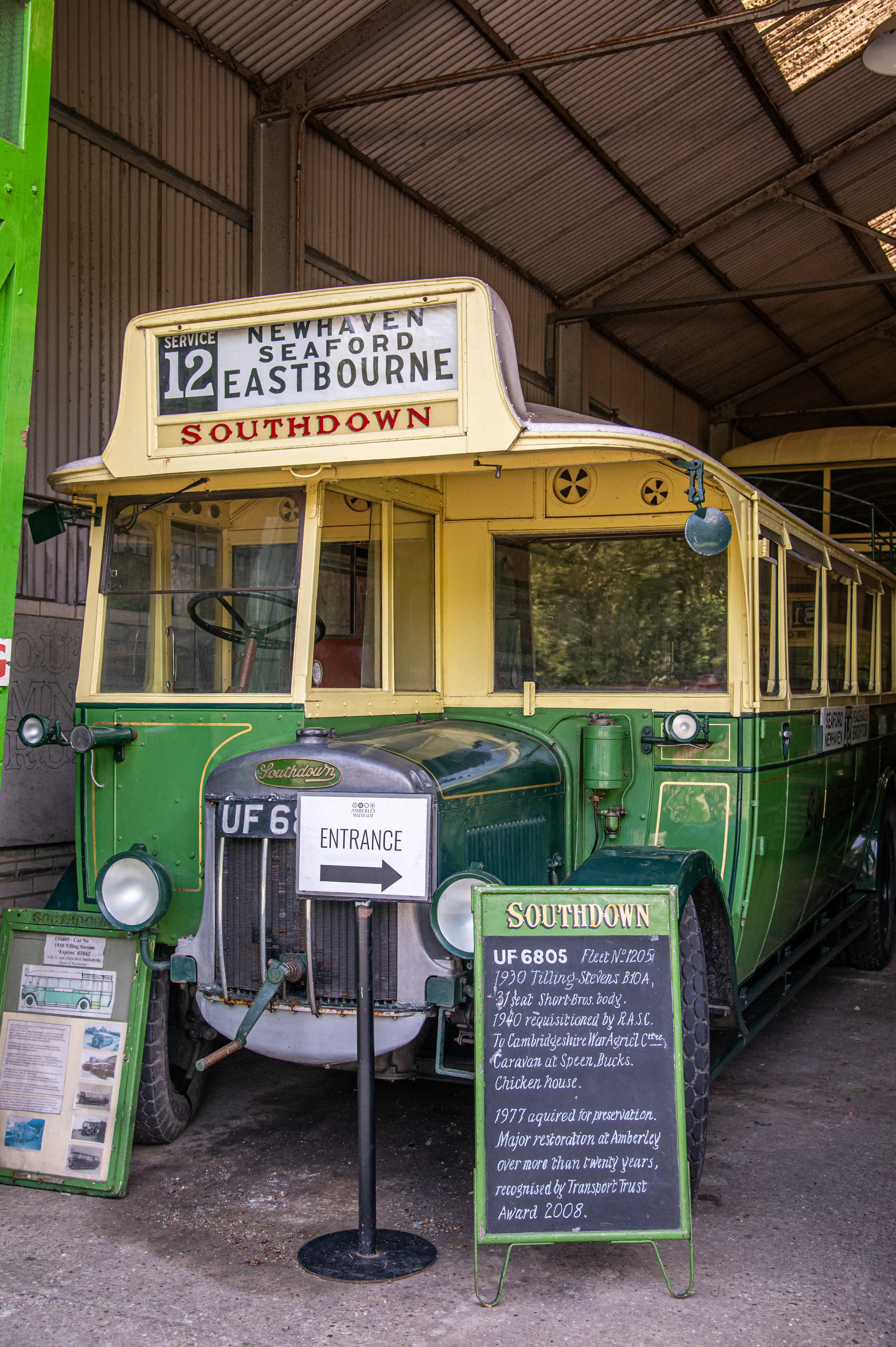 A vintage green and cream Southdown double-decker bus, registration UF 6805, with 'Southdown' lettering and route signs for Newhaven, Seaford, and Eastbourne, is parked indoors. Information boards and an entrance sign are visible in front of the bus.