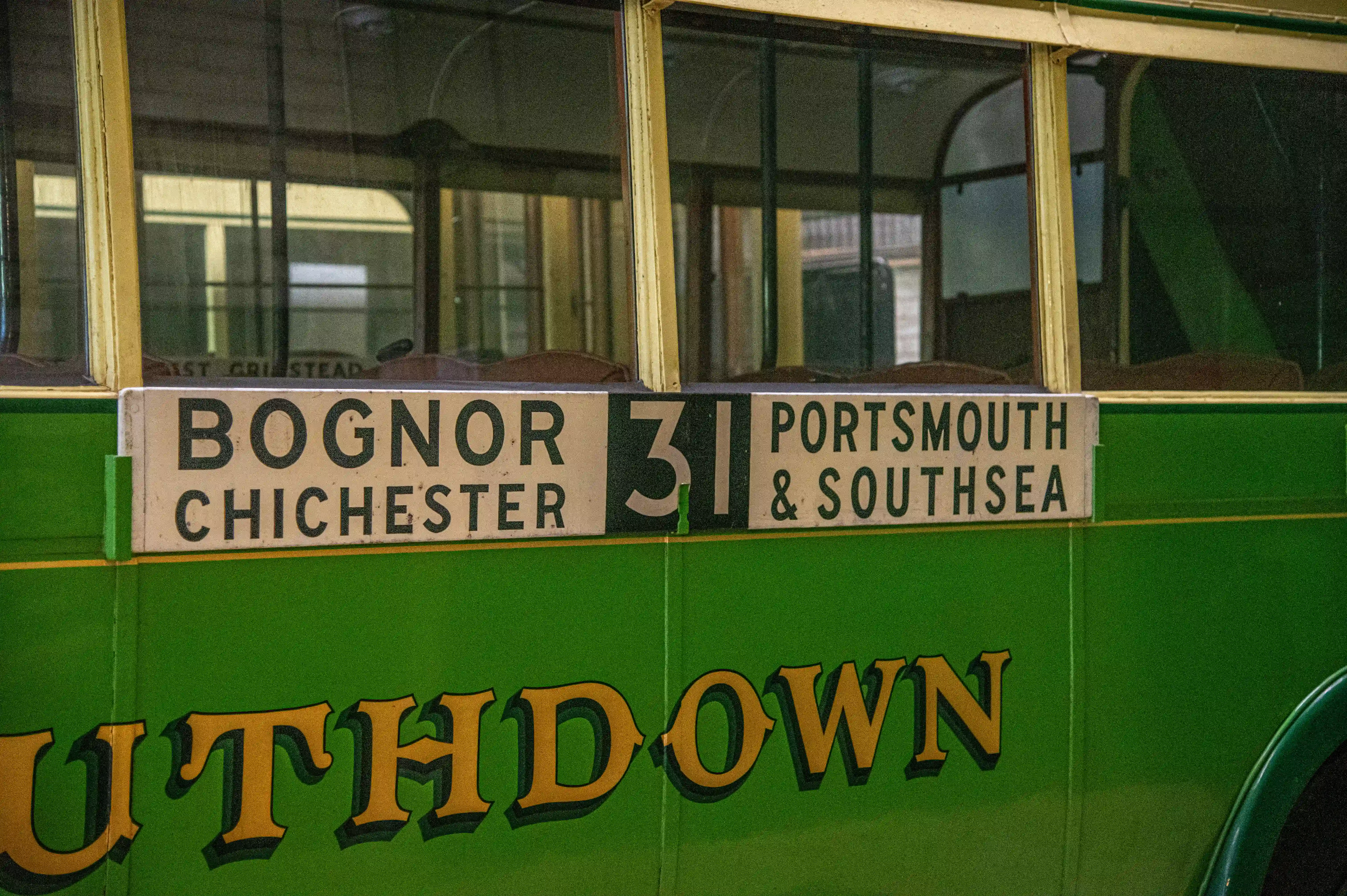Close-up of a vintage green bus showing a destination sign with 'BOGNOR CHICHESTER' and 'PORTSMOUTH & SOUTHSEA' and route number '31'. The company name 'SOUTHDOWN' is also visible.