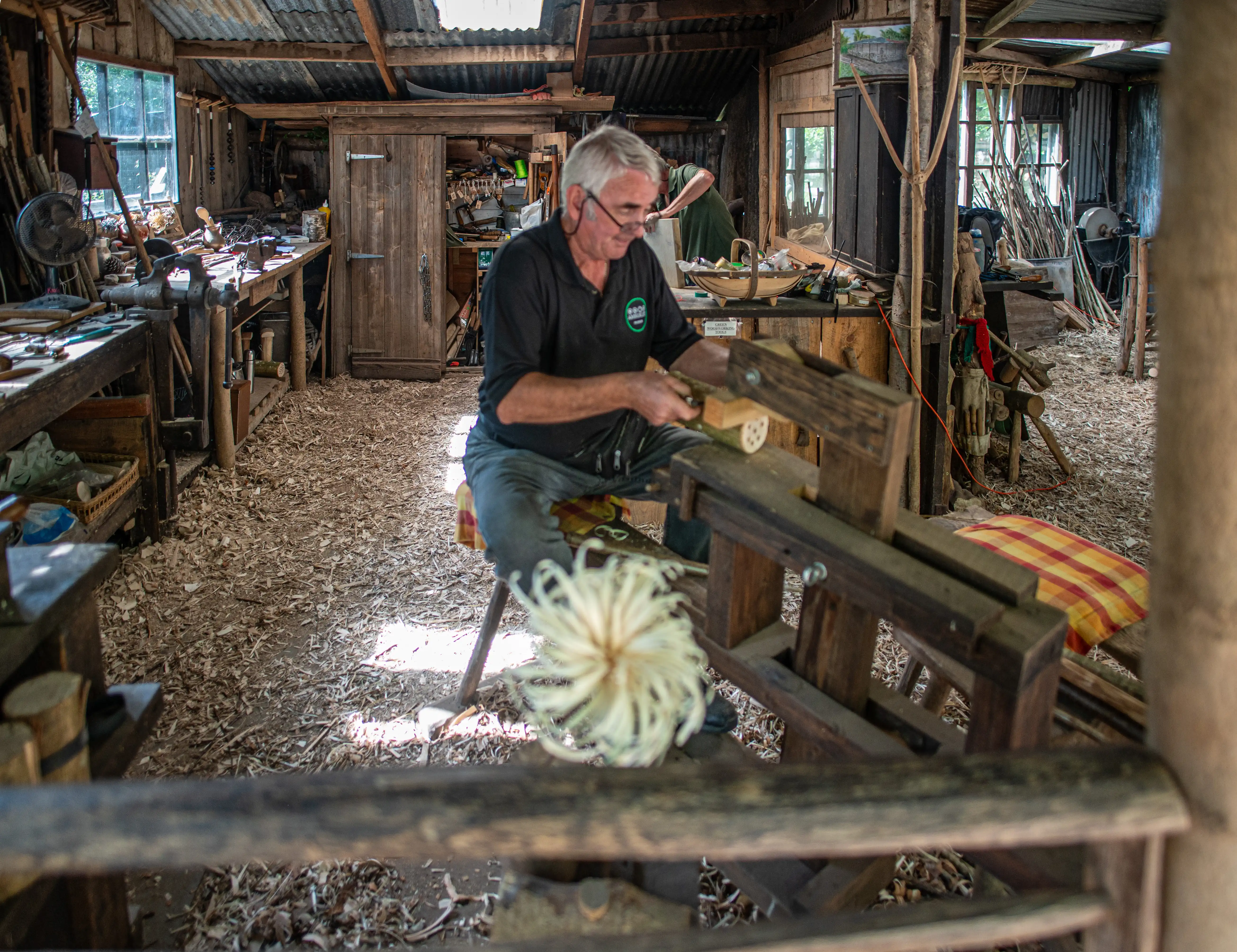 A man is using a lathe in a workshop with a corrugated iron roof.