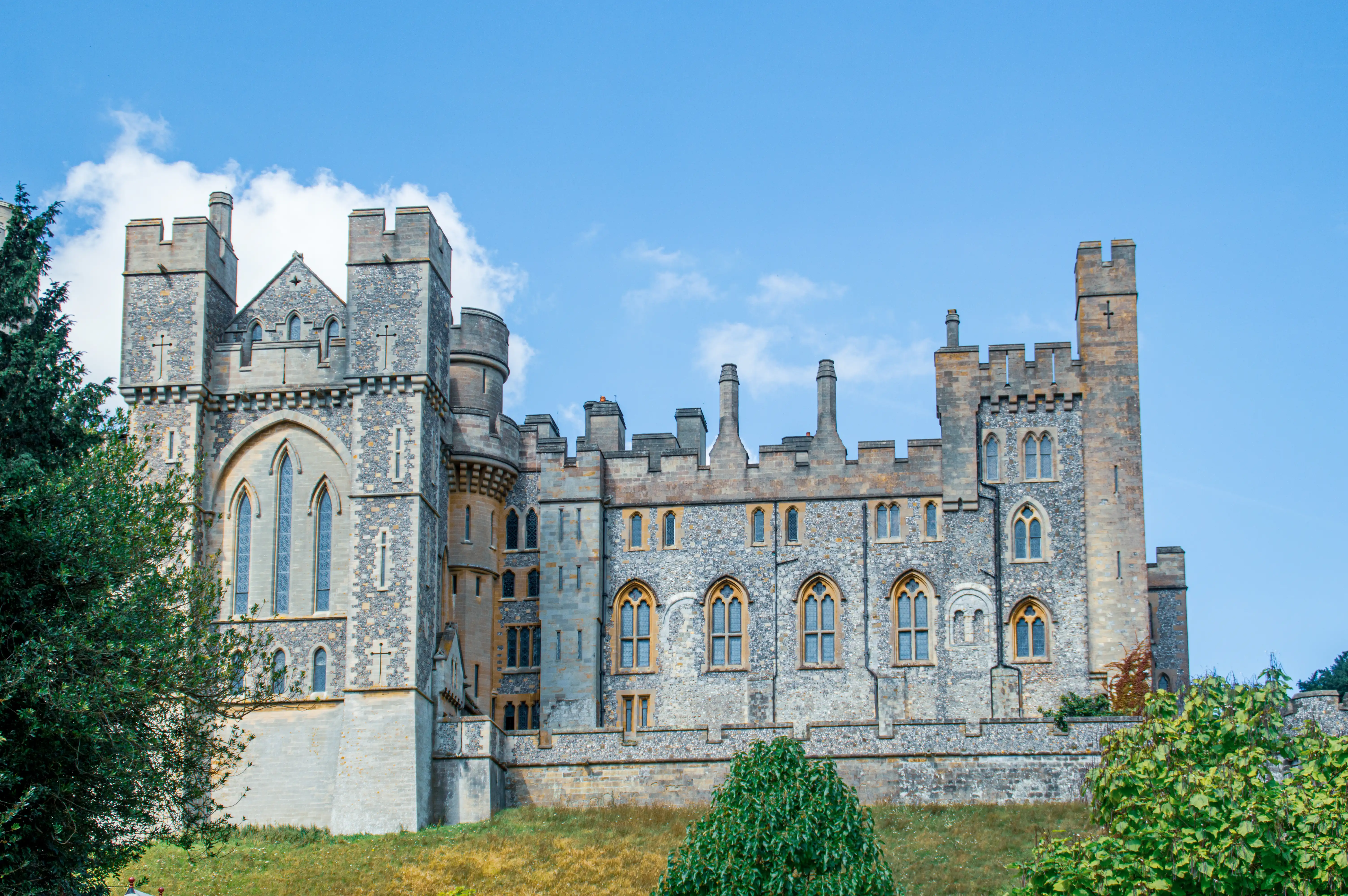 pointed-arch windows on a grassy hill under a clear blue sky.
