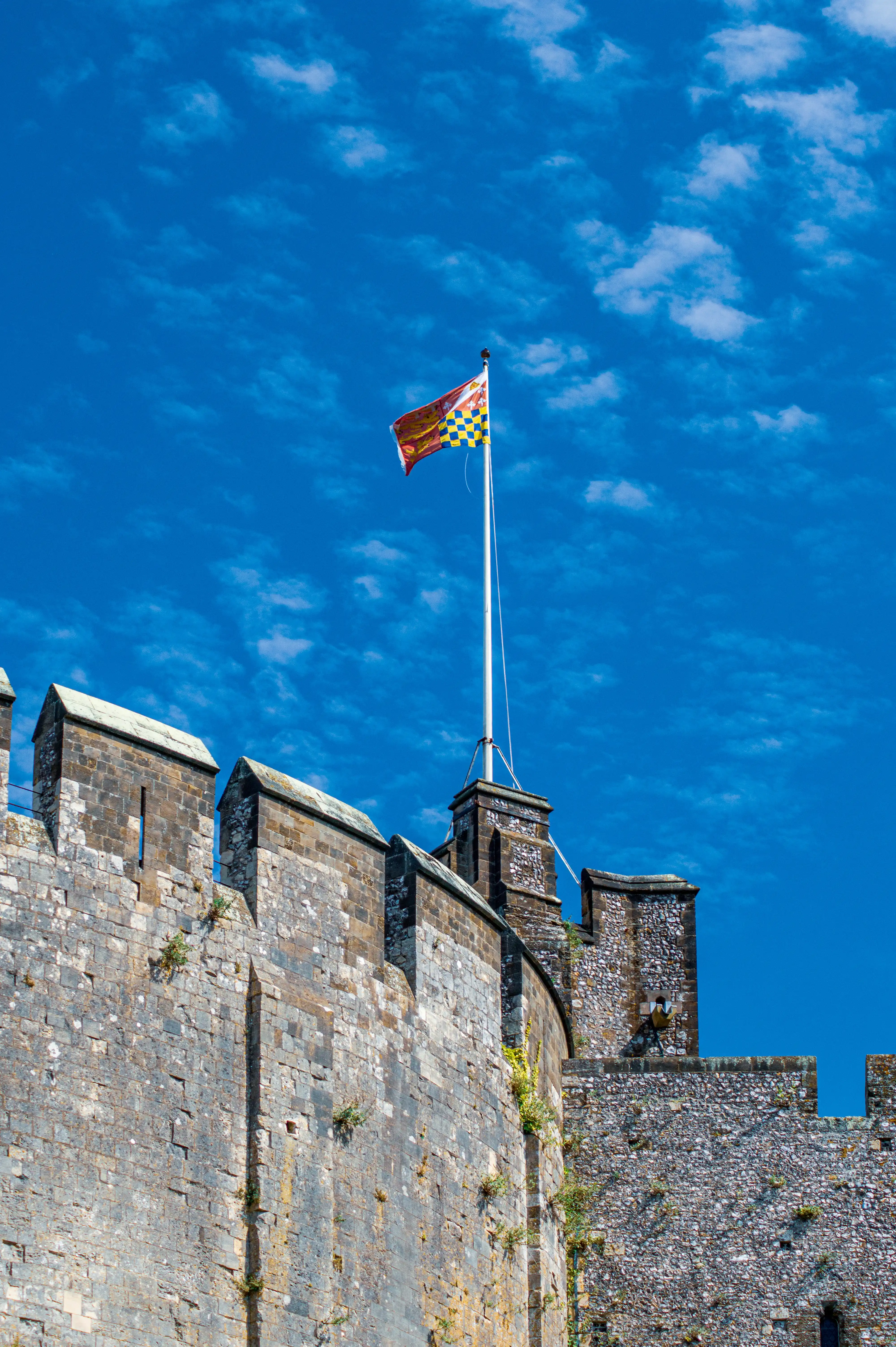 A photograph shows a castle with stone walls and battlements. A flagpole flies a colourful Royal Standard against a blue sky with white clouds.