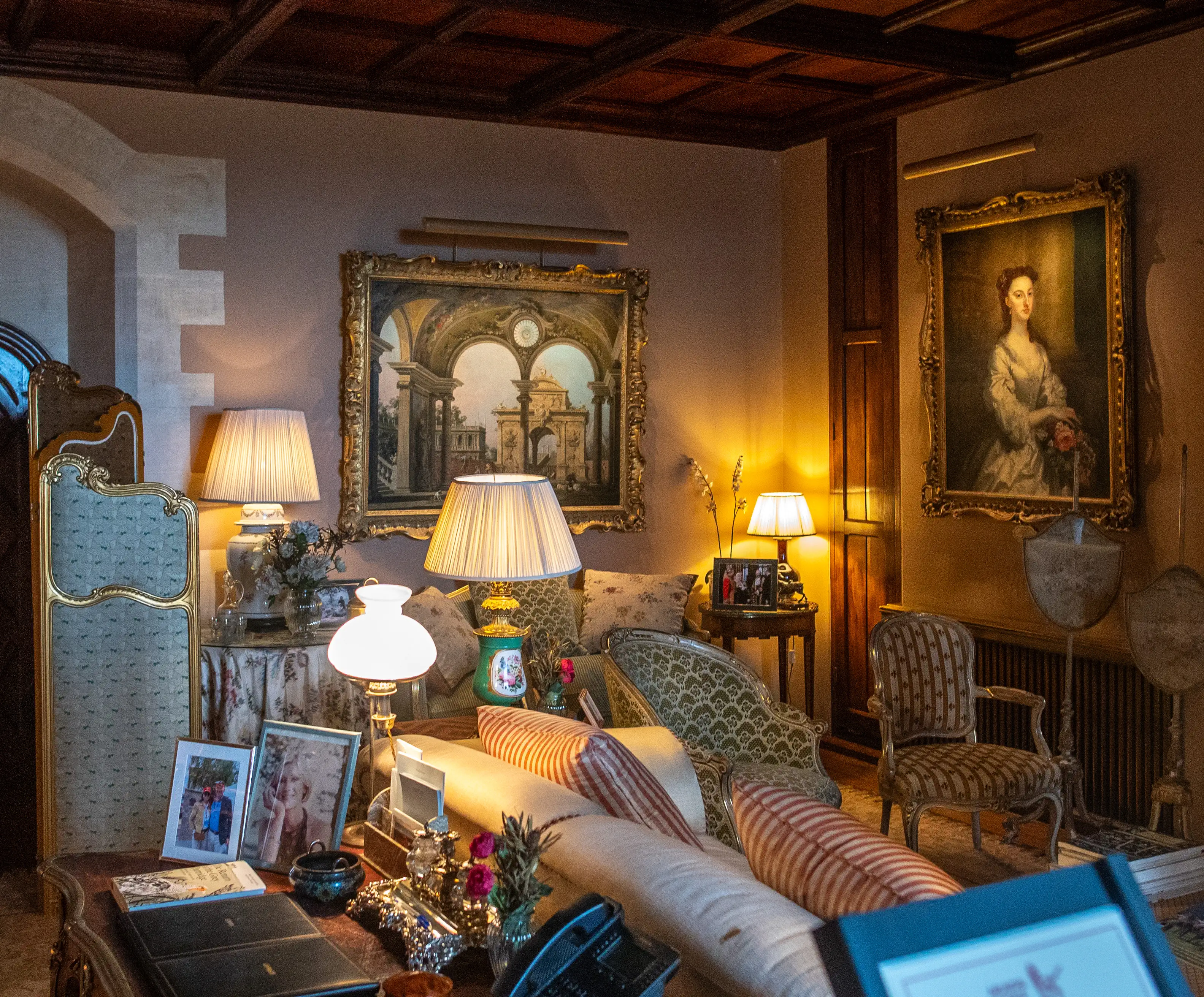 A formal sitting room in warm, ambient lighting, showcasing antique upholstered chairs and sofas, framed classical paintings, and decorative table lamps.