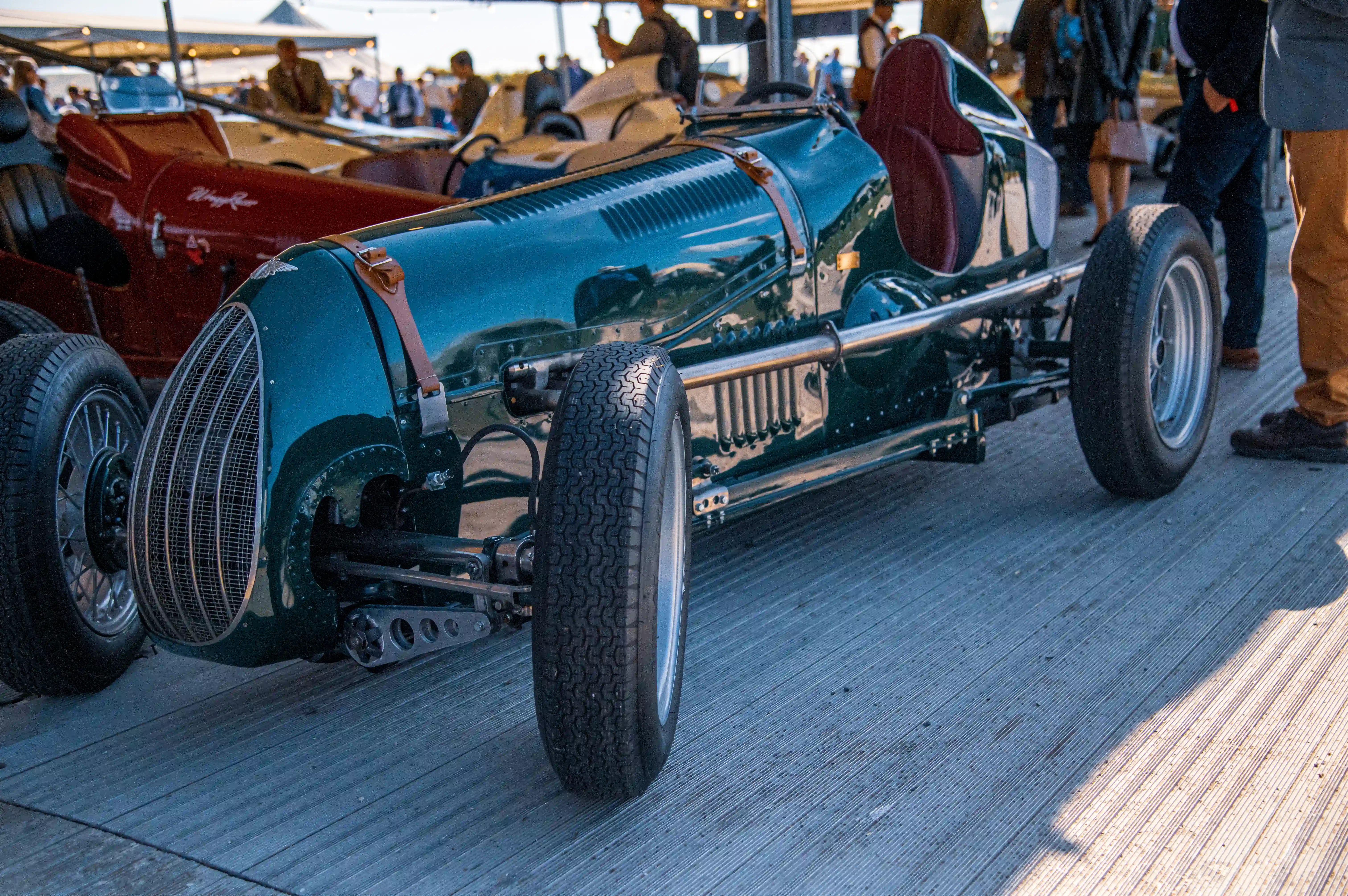 Close-up of a gleaming, dark green vintage racing car with exposed front wheels and a prominent grille, parked on a wooden deck.