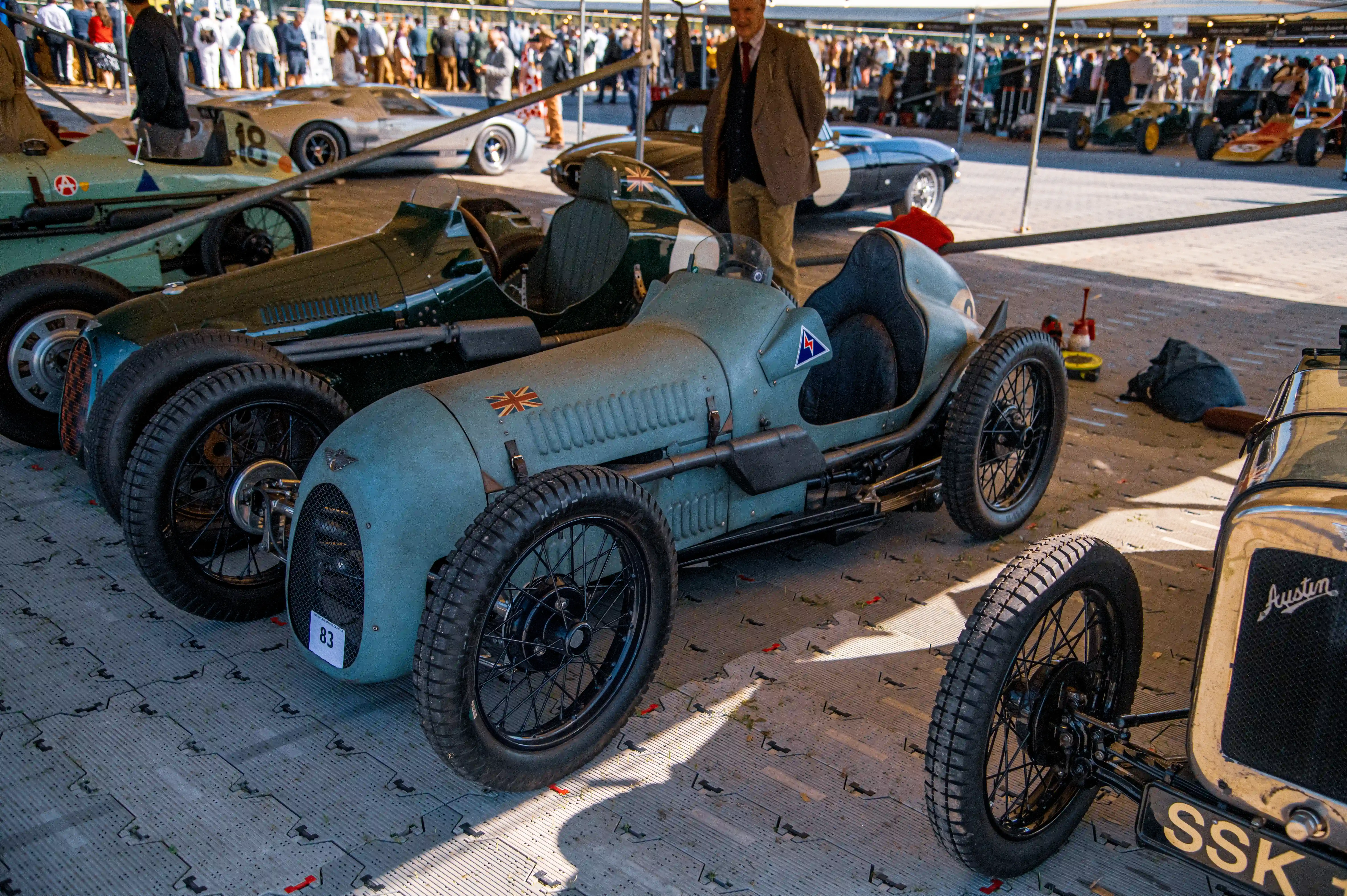 Close-up view of vintage racing cars lined up, with the prominent blue car in the foreground featuring a Union Jack and race number 83.