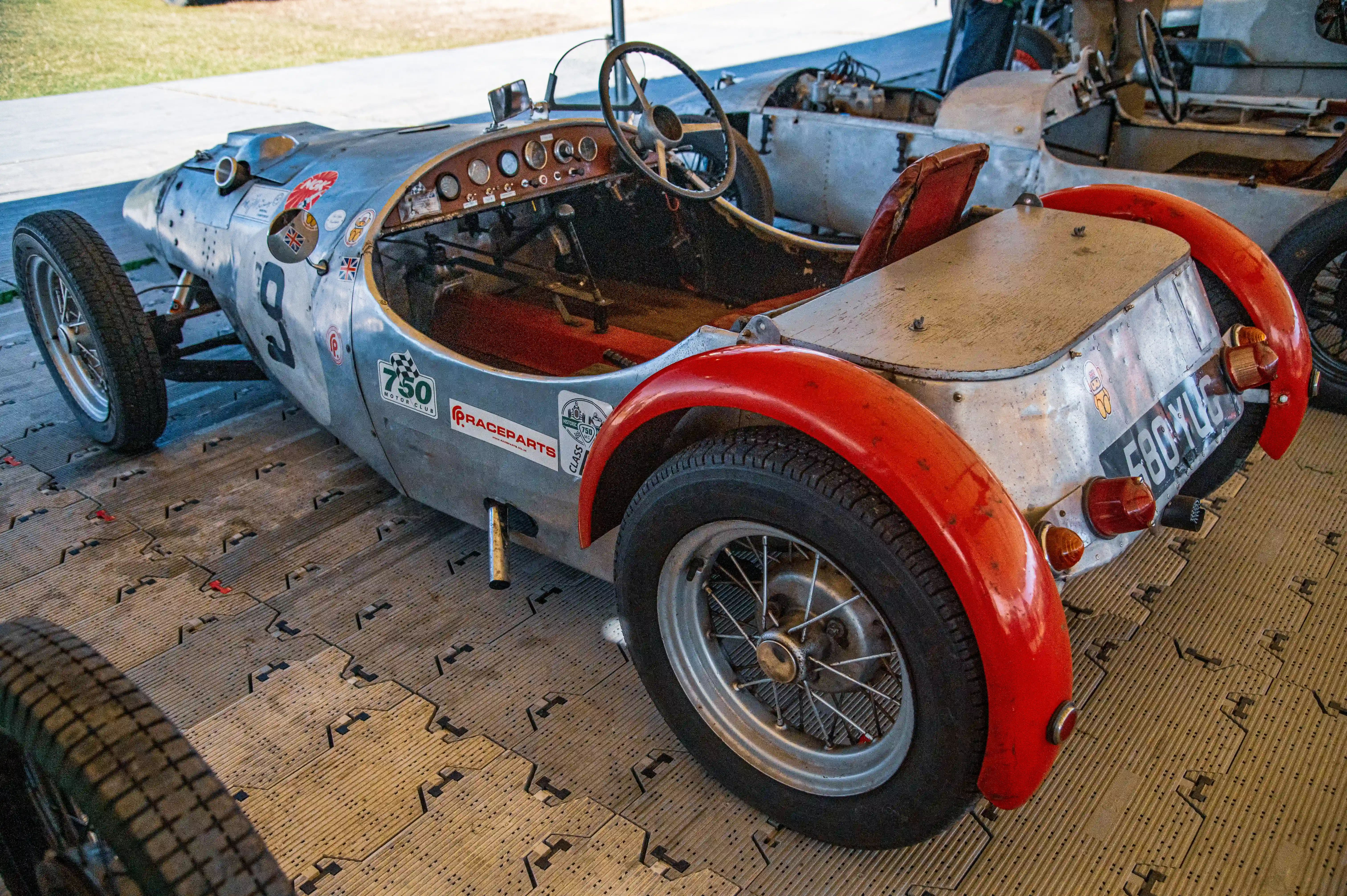 A vintage silver racing car with red wheel arches and the number 9 on its side, viewed from a low angle.