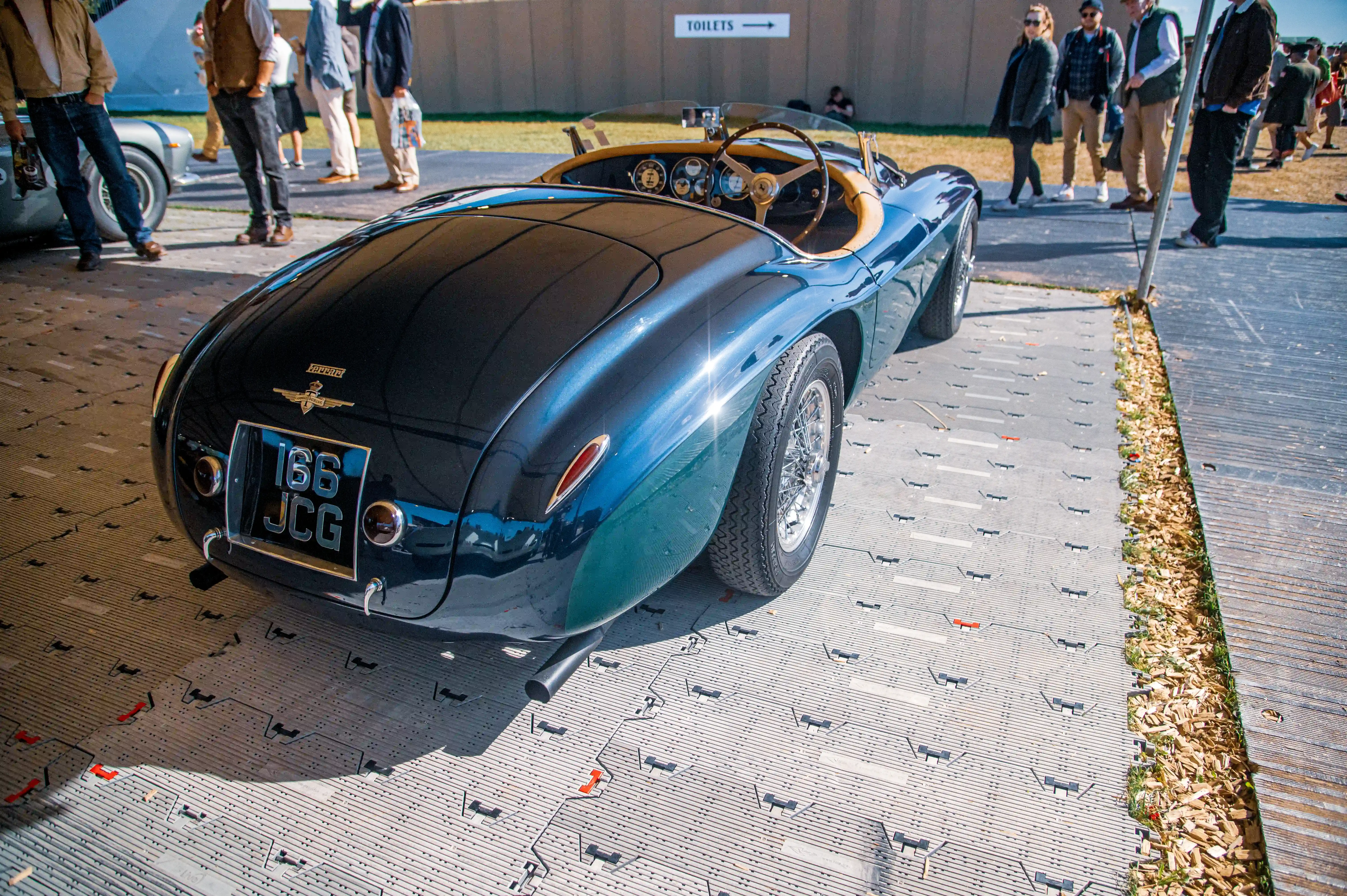 Rear view of a gleaming dark green vintage Ferrari convertible with a UK license plate 