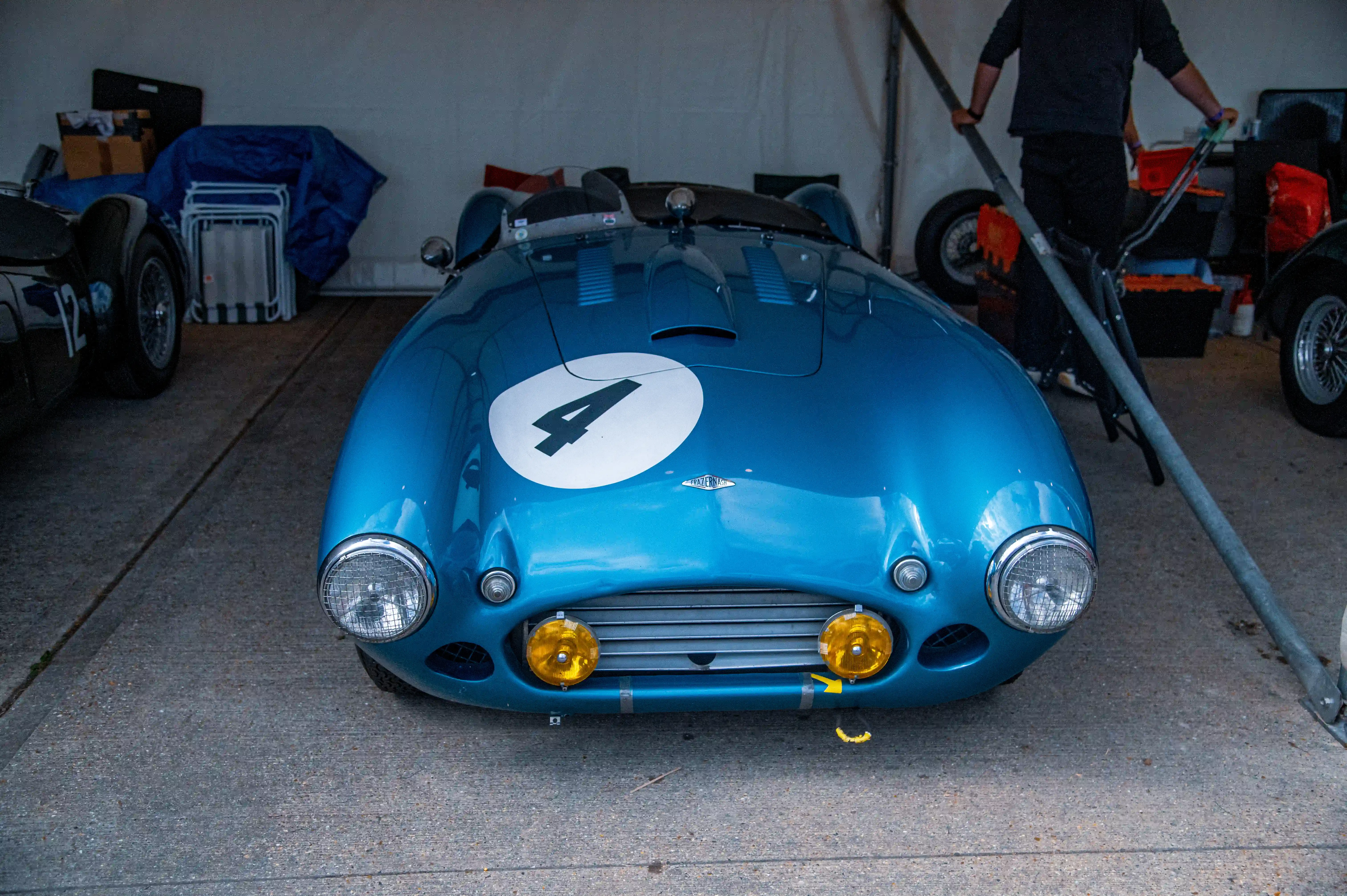 Front view of a vintage blue racing car with a white circle and the number 4 on the bonnet, featuring yellow fog lights and round headlights.