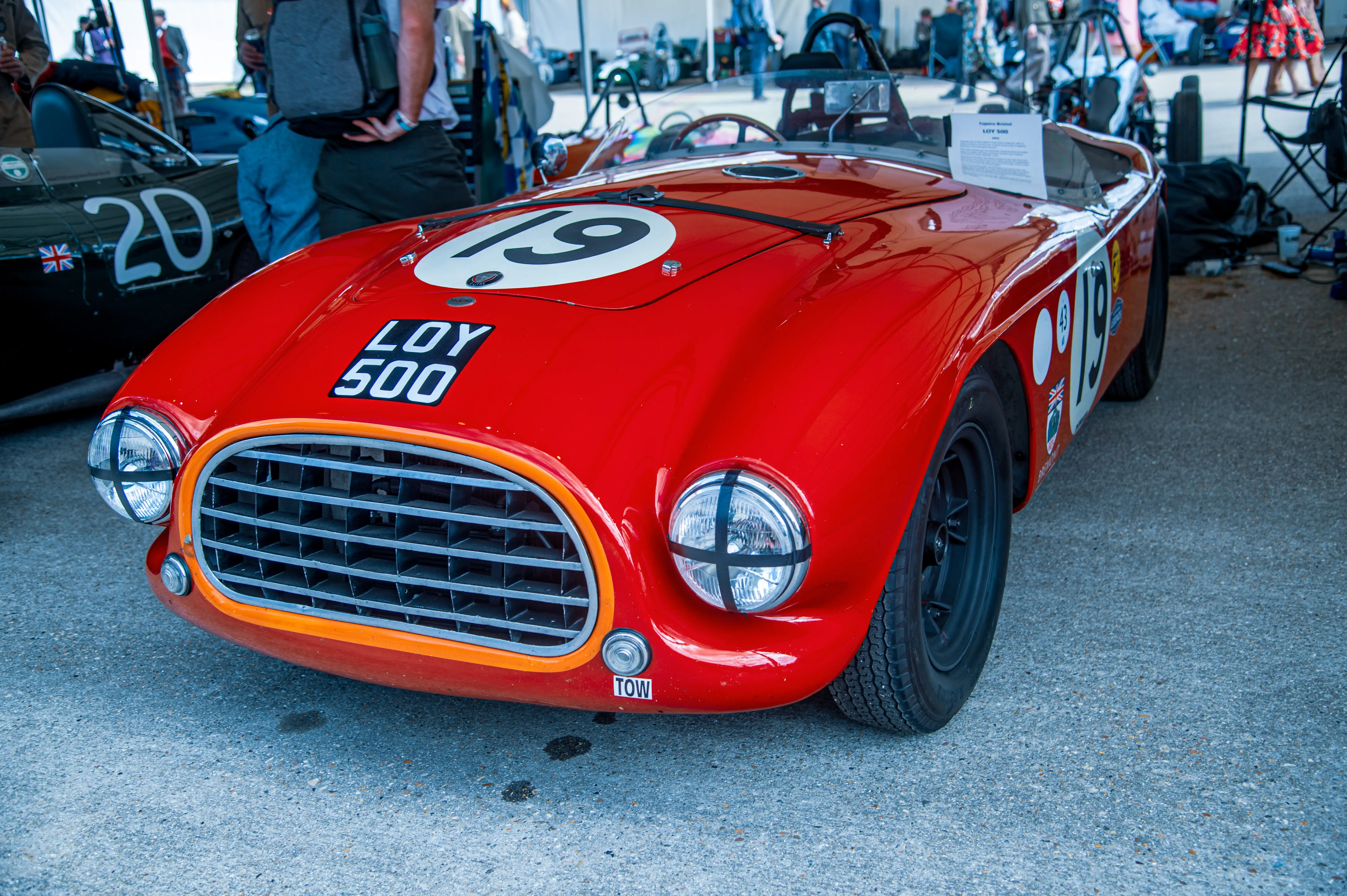 Close-up front view of a bright red classic racing car with a silver grille and number '19' on the bonnet. A small 'TOW' sticker is visible near the front bumper.