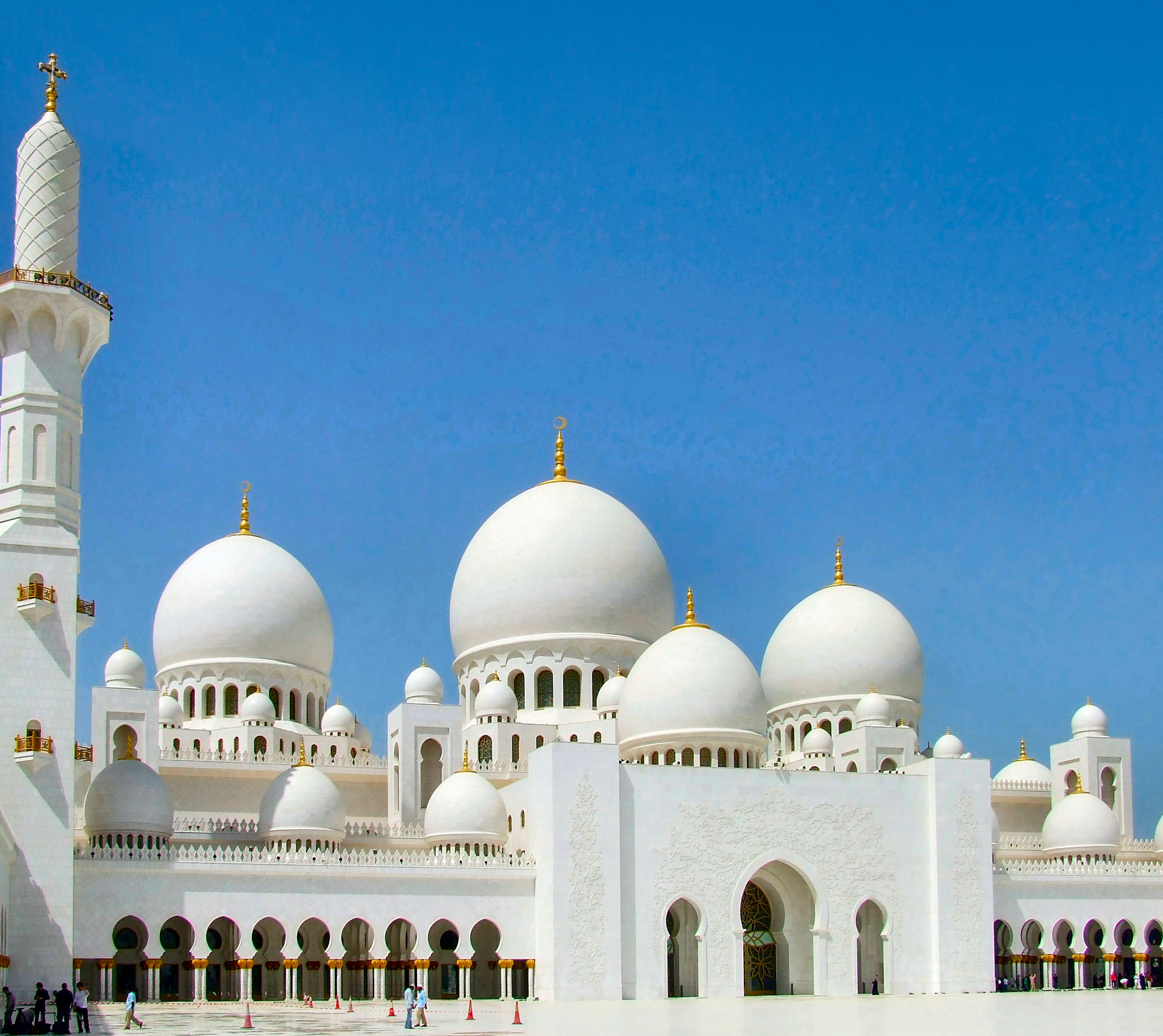The mosque's exterior is predominantly white, reflecting the bright sunlight and contrasting beautifully with the clear blue sky